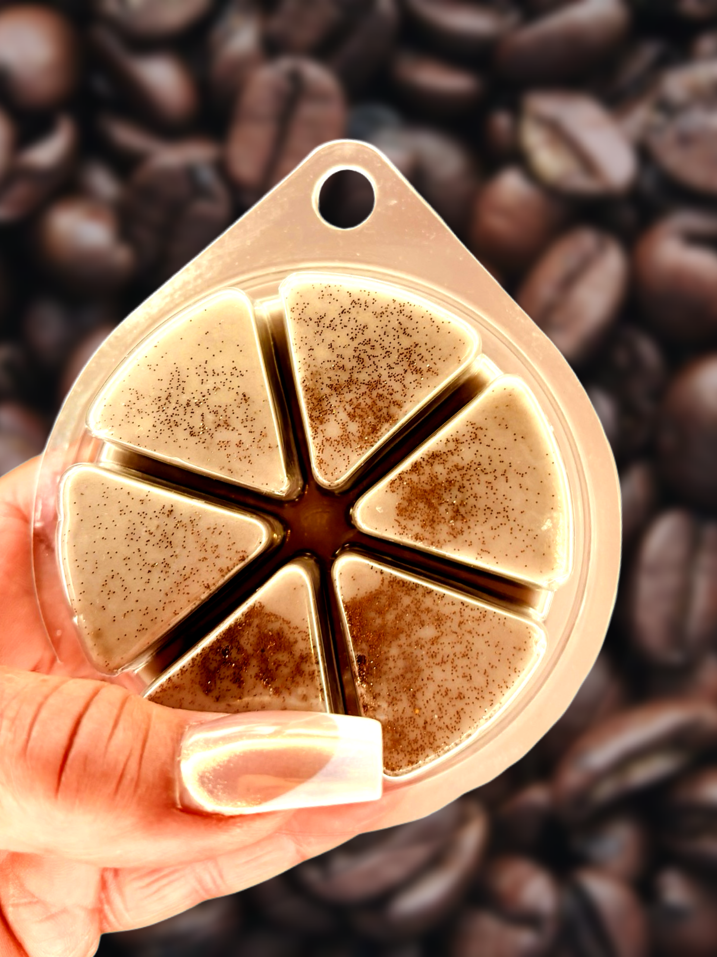 A hand holds The Soap Gal x's The Morning Coffee Run Wax Melt 85g, featuring six creamy caramel-scented wedges against a backdrop of roasted coffee beans, evoking the essence of a morning coffee run.