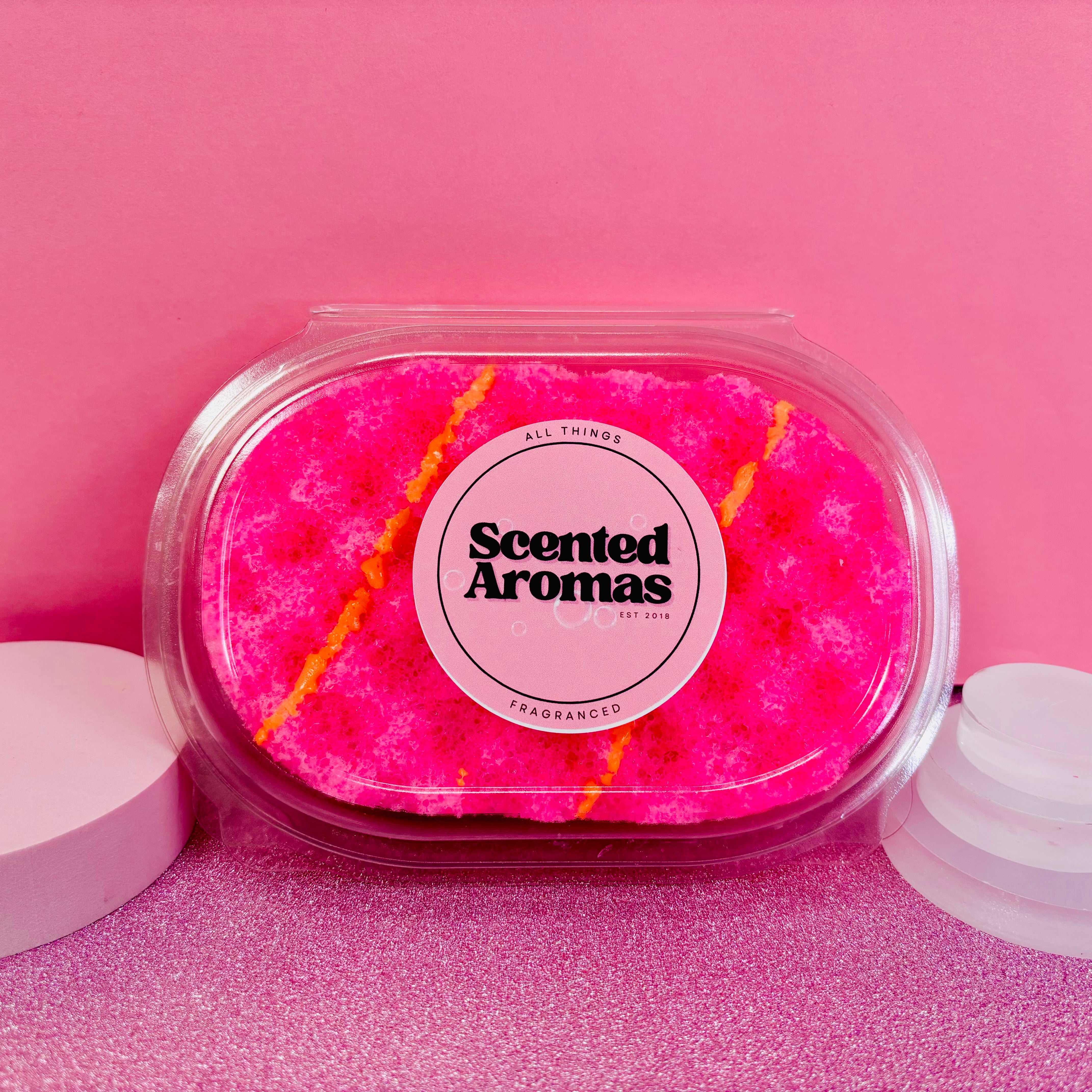 A pink and yellow Pink Lemonade Exfoliating Soap Sponge from The Soap Gal x, presented in clear packaging, is set against a pink background.