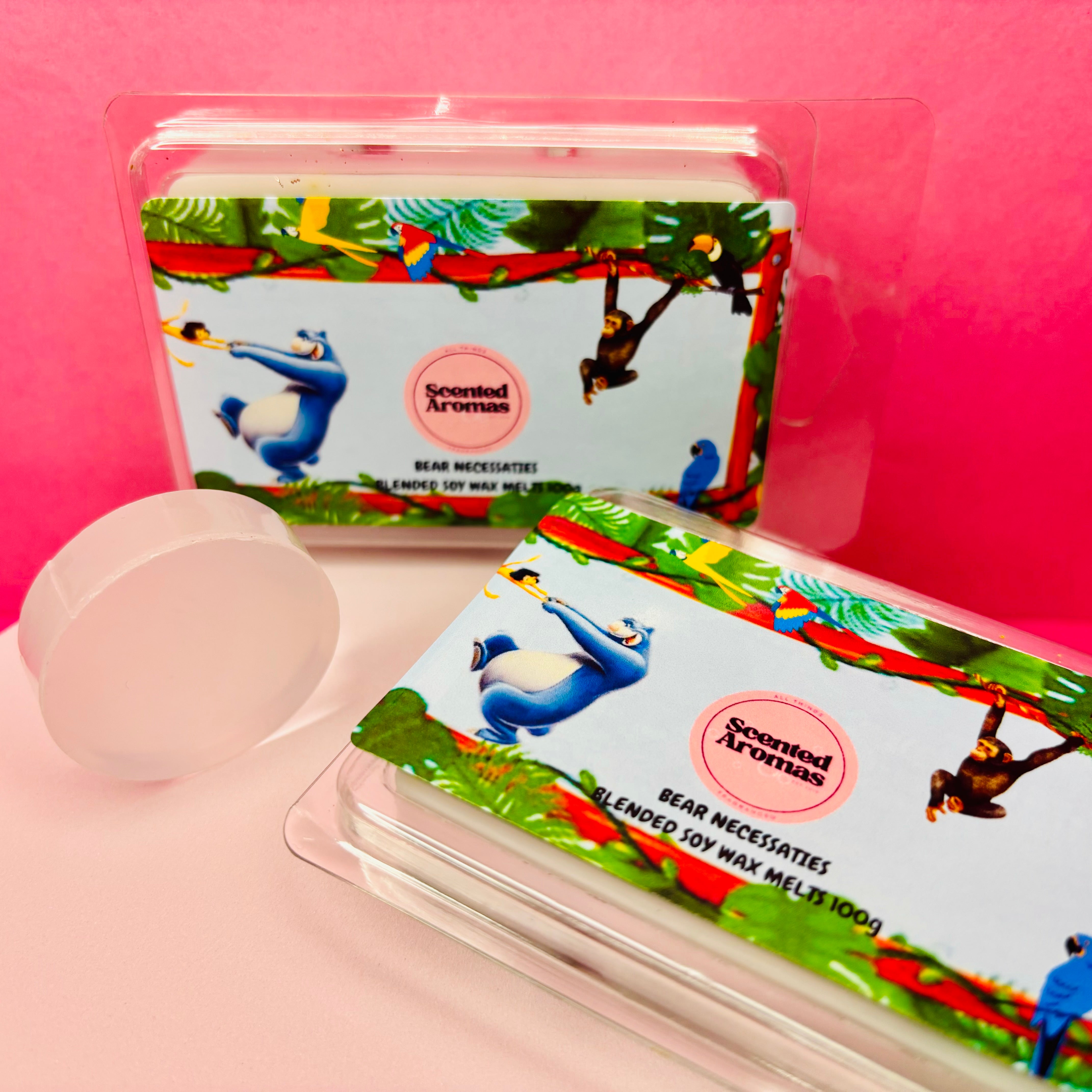 Two packages of "All You Need Is the Absolute Necessities" scented soy wax melts by The Soap Gal x, infused with essential oils and featuring colorful jungle-themed packaging set against a pink background.