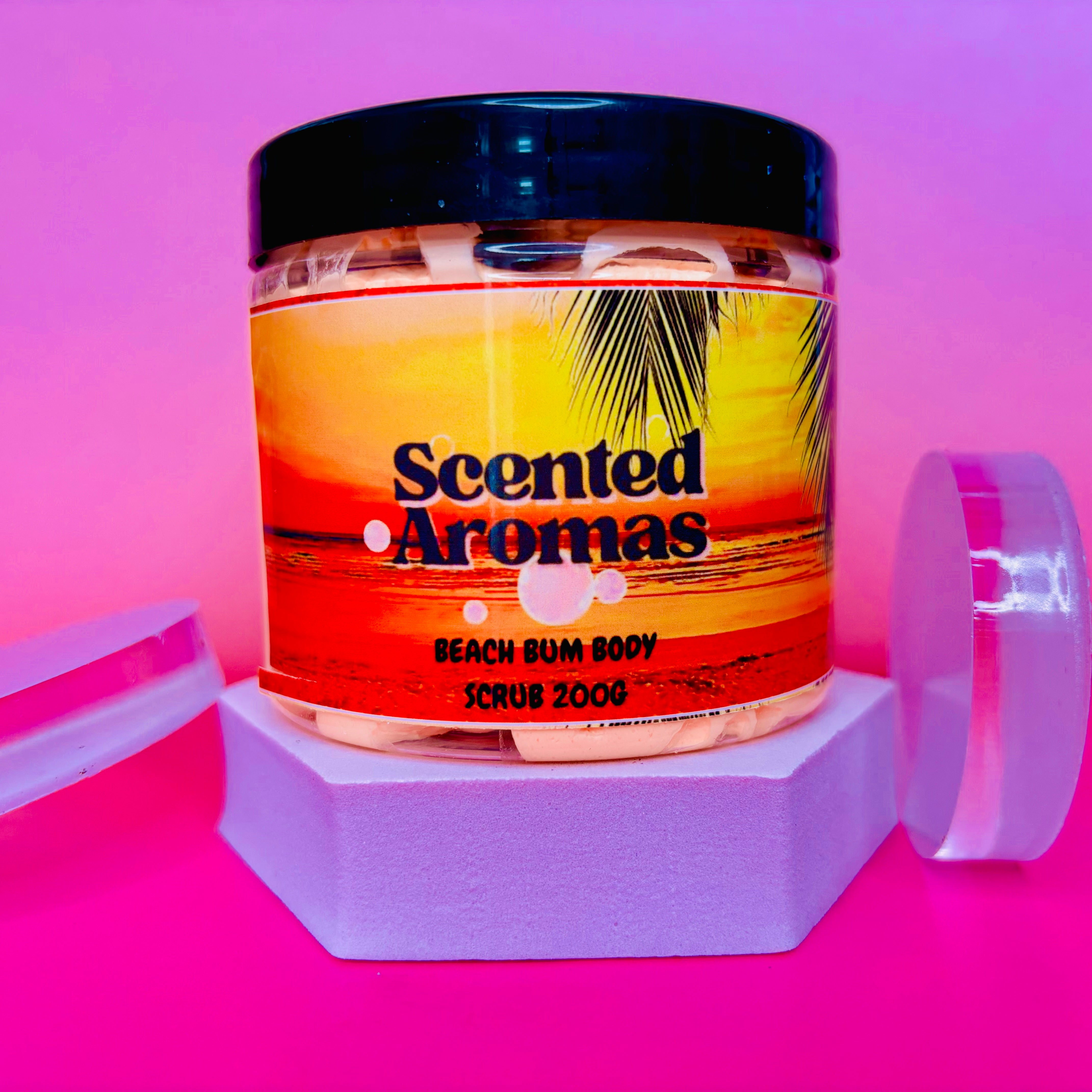 A jar labeled "The Soap Gal x Brazilian Bum Cream Whipped Soap Shave Butter 200g" rests on a white stand amid a pink and purple backdrop, reminiscent of the indulgence found in Brazilian Bum Cream.