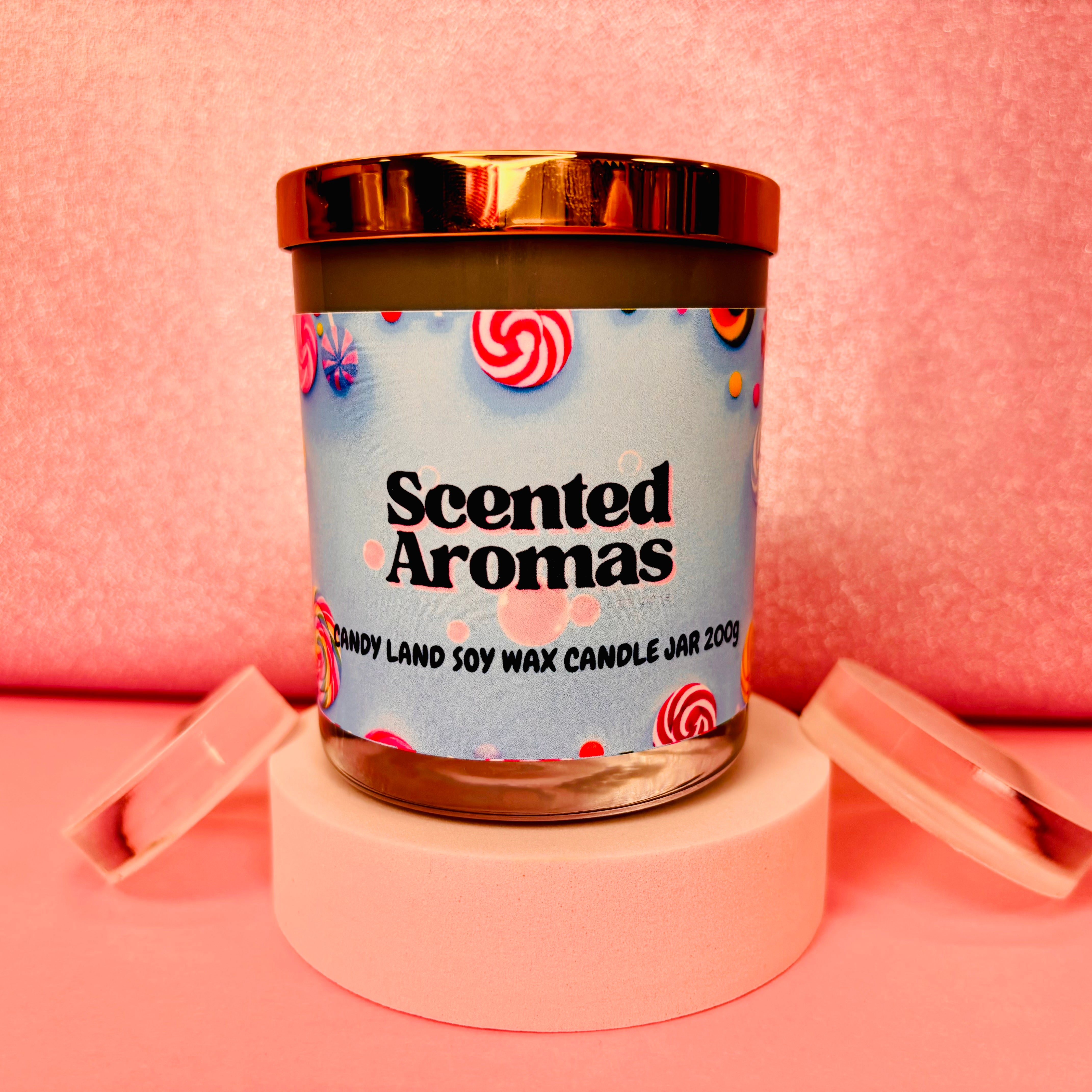 A 200g "Candy Land Candle" from The Soap Gal x rests elegantly on a circular stand against a pink background.