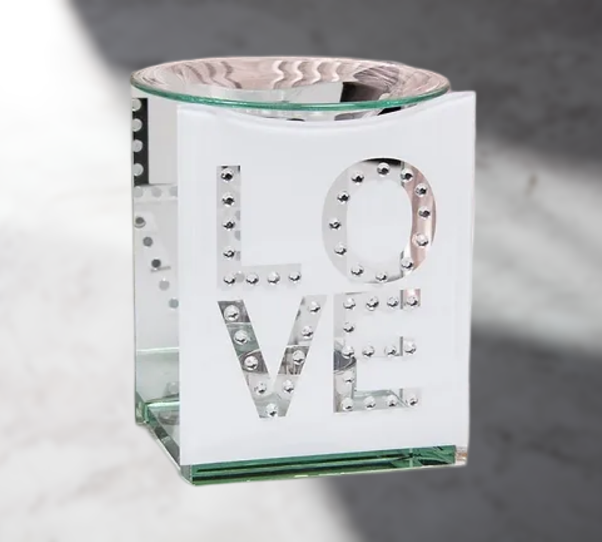 The Soap Gal x's Glass Love Printed Wax Warmer is a limited edition piece with "LOVE" creatively cut out in large letters, designed as a white glass candle holder that also functions as an elegant fragrance oil burner, enhancing any space with its charm.