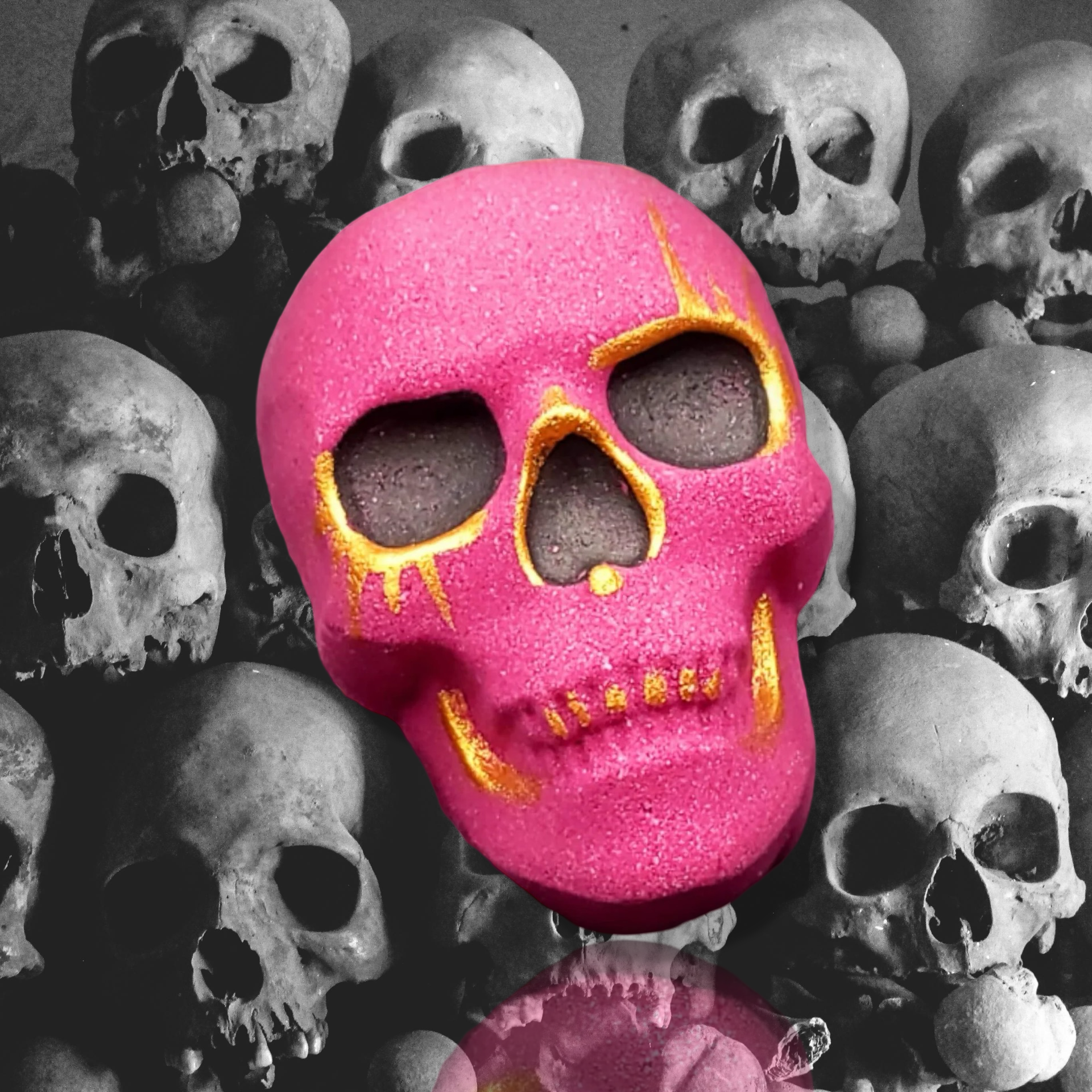 Introducing the limited edition Hector Skeleton Bath Bomb by The Soap Gal x, showcasing a vibrant pink skull adorned with dark eye sockets and shimmering gold accents, all set against a grayscale backdrop of multiple skulls.