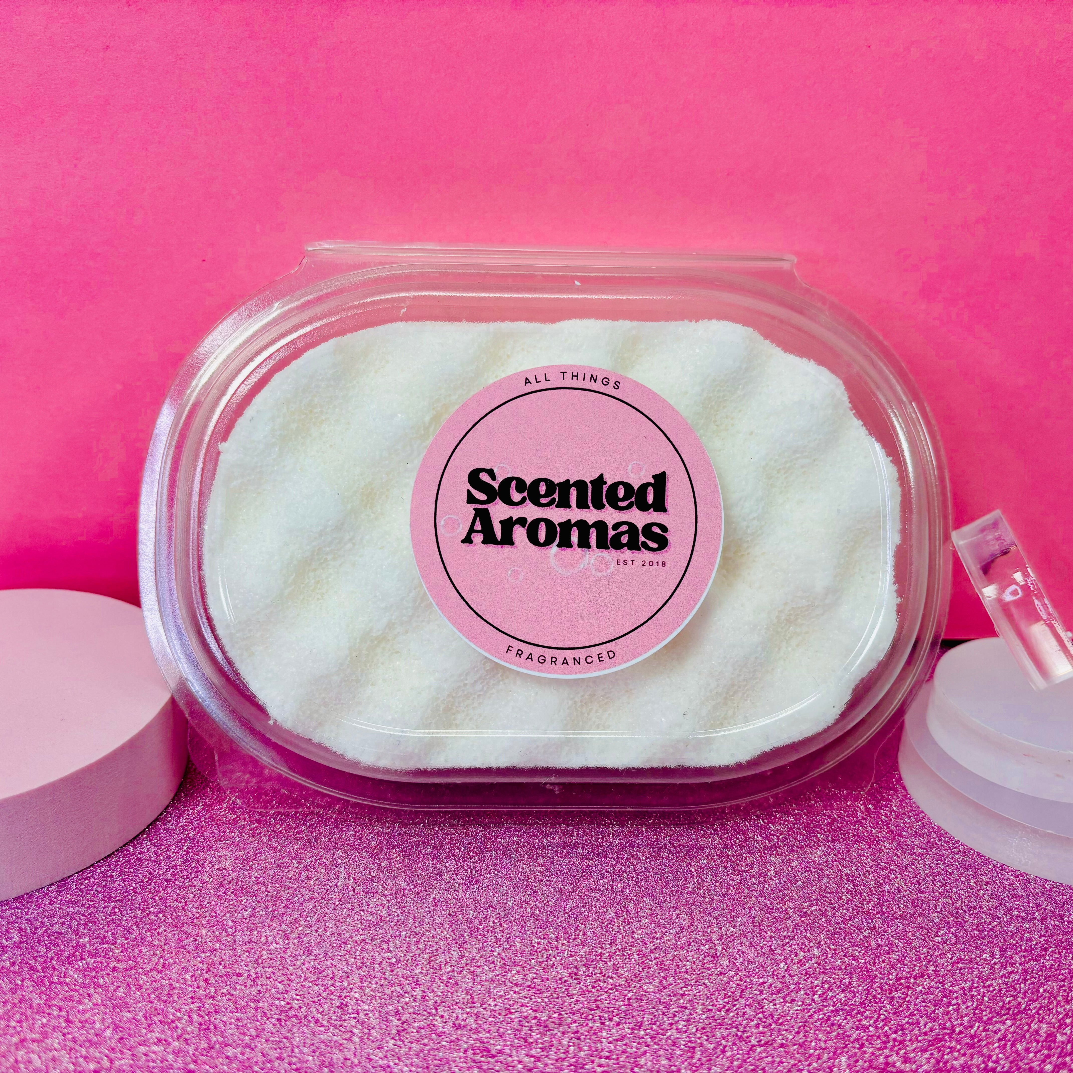 A white, wavy exfoliating soap sponge from "The Soap Gal x," named "Clouds Exfoliating Soap Sponge," is showcased in a clear plastic container against a pink background, ideal for Manchester's skincare enthusiasts.