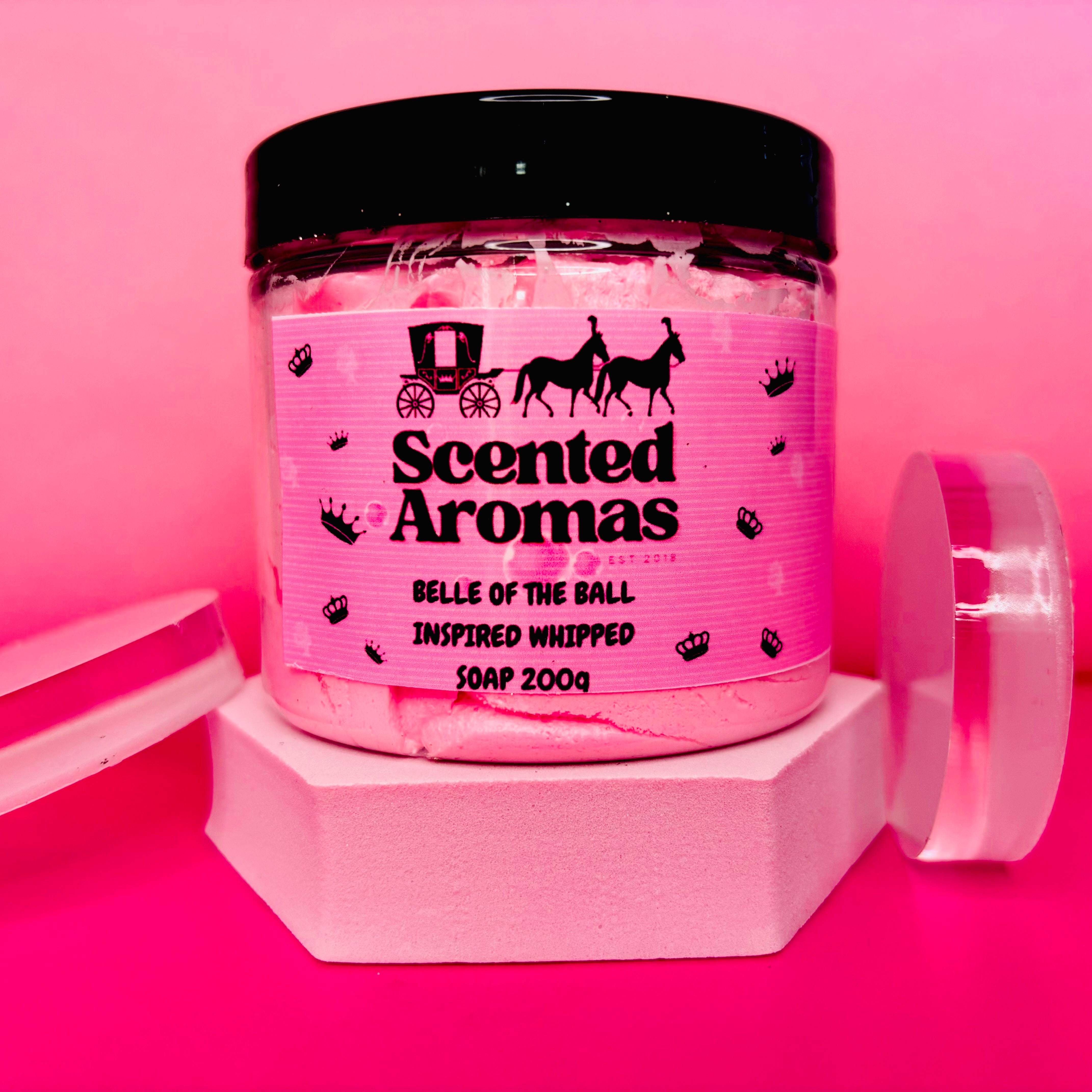 A jar of pink whipped soap labeled "The Soap Gal x: Belle Of The Ball Whipped Soap Shave Butter 200g" with a hydrating formula sits elegantly against a pink background, evoking the essence of La Vie Est-inspired perfume.