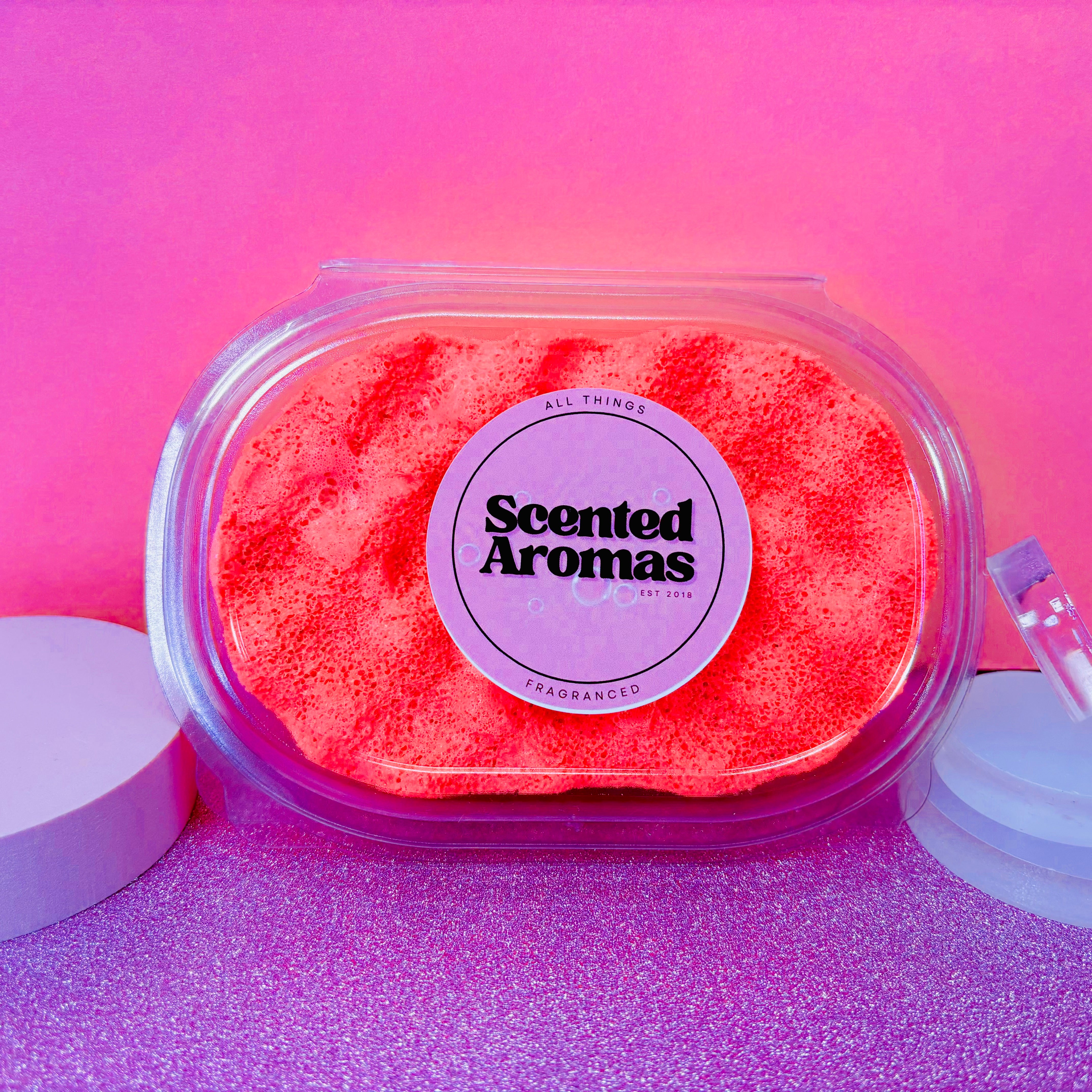 The "Opium Exfoliating Soap Sponge" by The Soap Gal x, encased in a clear container crafted from recycled plastic, features an oriental fragrance set against a pink background.