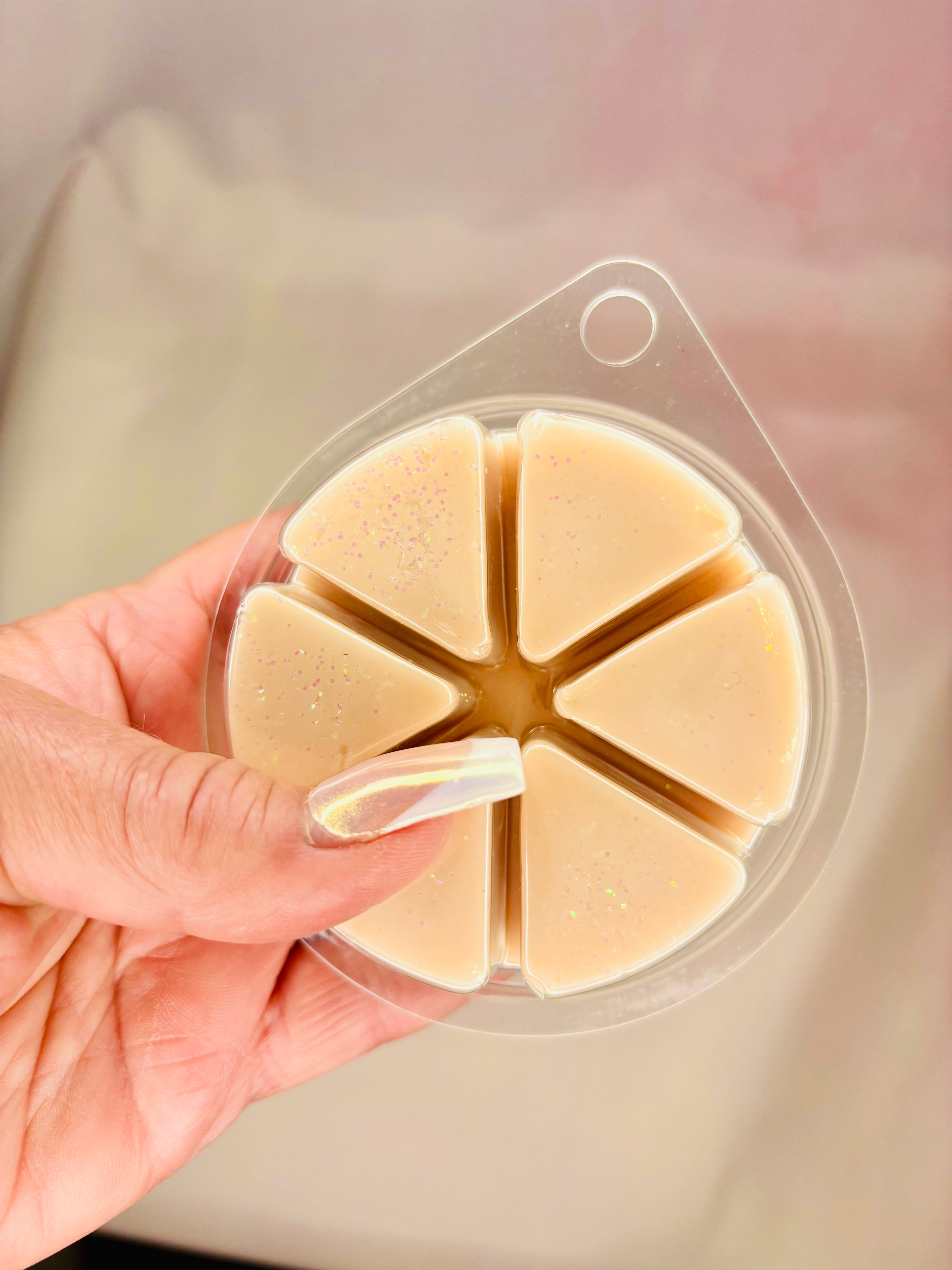 A hand holds a round plastic container of The Soap Gal x Cashmere Glow Wax Melt, 85g, featuring six segments of beige, vegan-friendly wax melts that sparkle subtly and emit the soothing scent of Cashmere Glow.