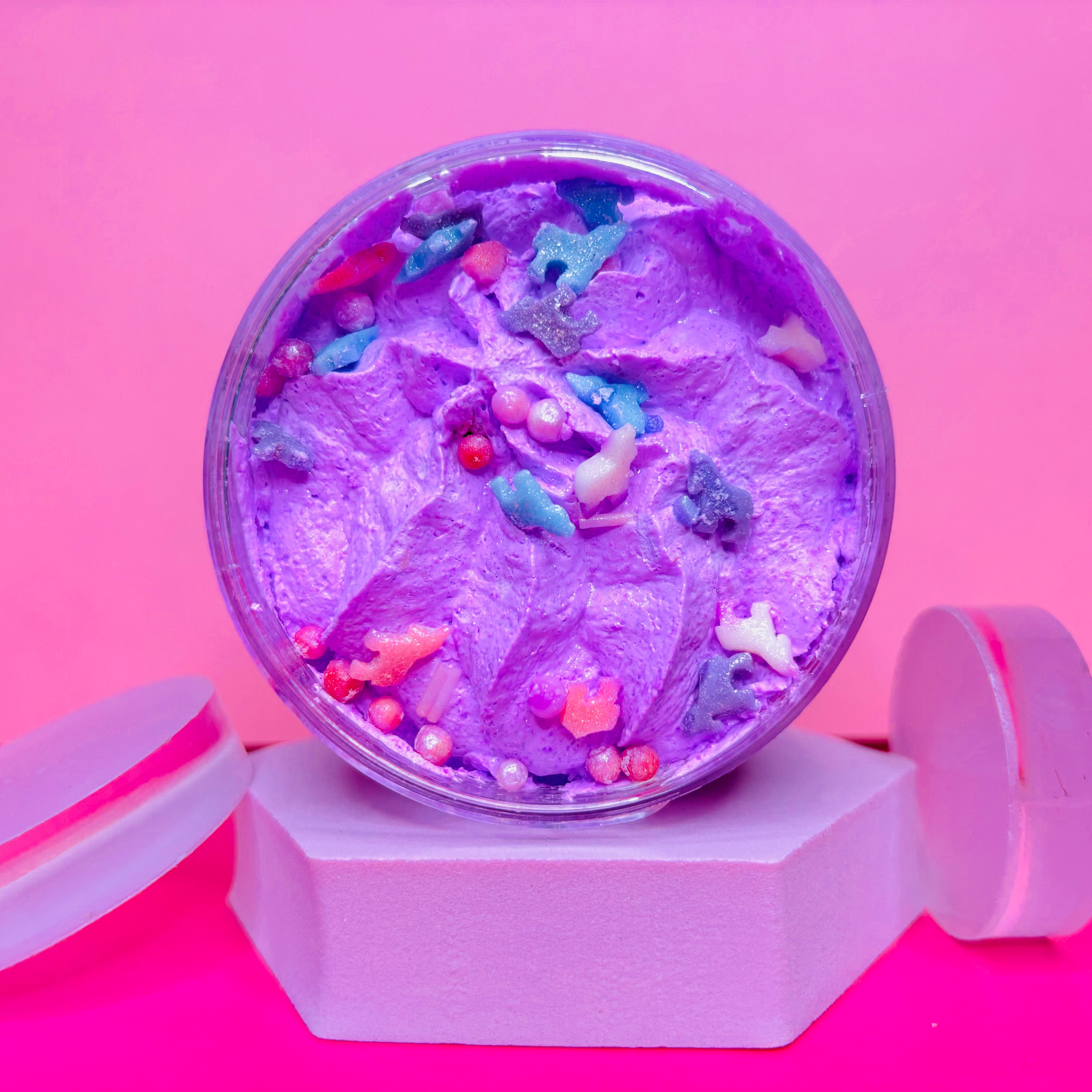 A container of purple whipped cream with colorful sprinkles, on a hexagonal platform similar to a birthday cake bath bomb against a pink background; part of Scented Aromas' Valentines Gift Set Bundle - 5 Beauty and Home Fragrances, perfect for a pamper night.