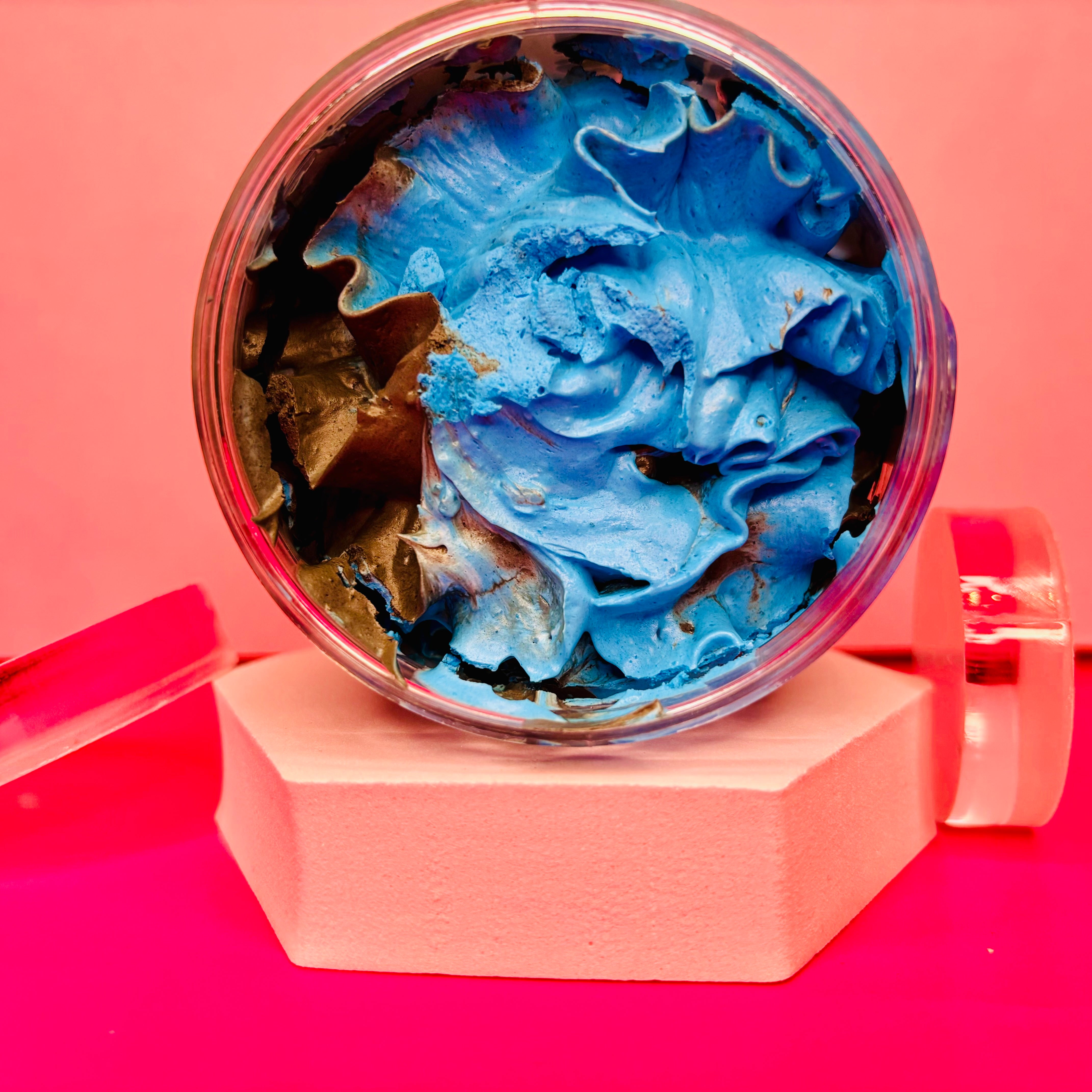 A jar of Kreed Whipped Soap Shave Butter, a luxurious men's grooming essential by The Soap Gal x, is elegantly displayed on a white hexagonal stand against a pink background.