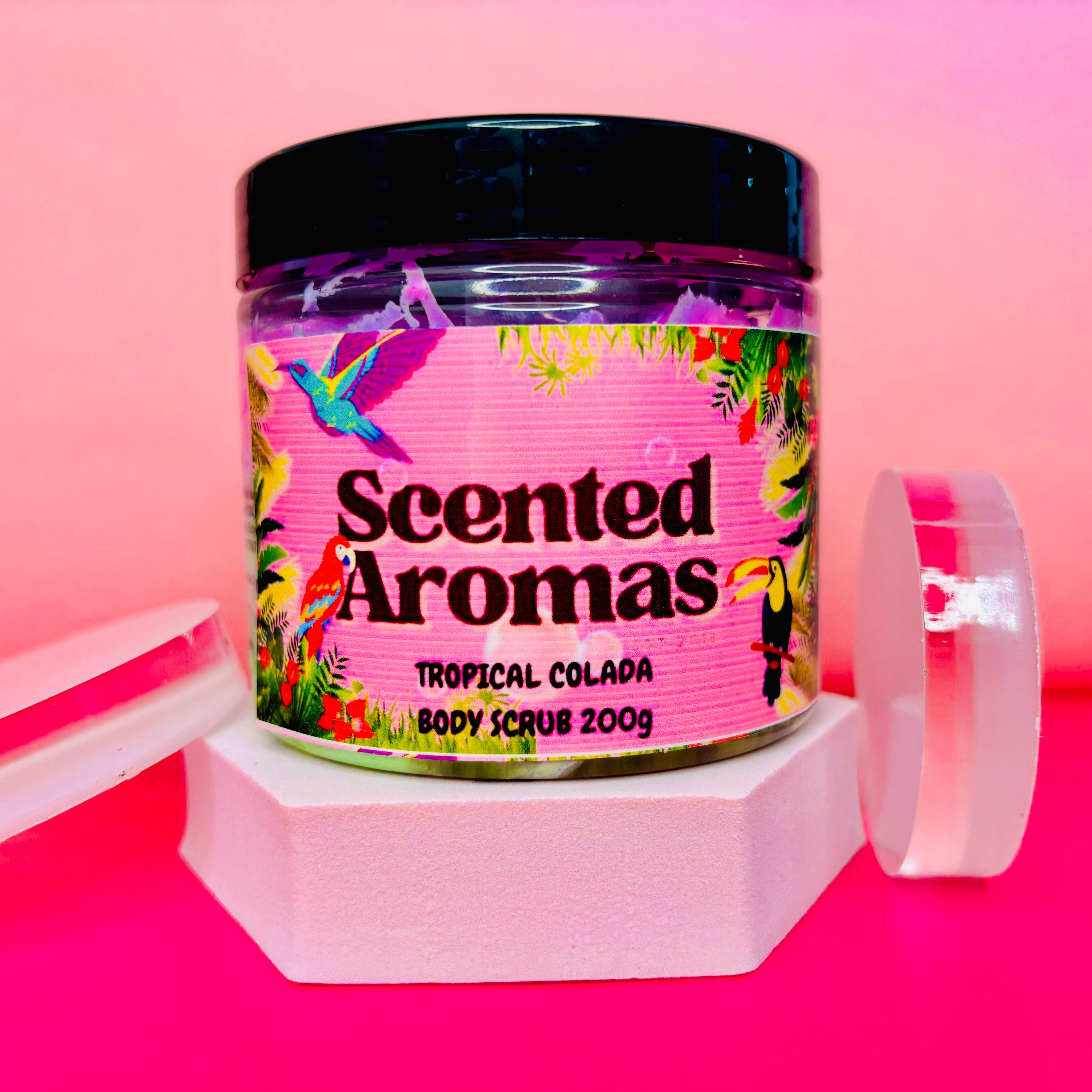 A jar of The Soap Gal x Unicorn Fluff Body Scrub, 200g, featuring a pink tropical-themed label, sits on a pink backdrop, capturing the refreshing essence of paradise. This delightful blend is perfect for smoothing your skin.