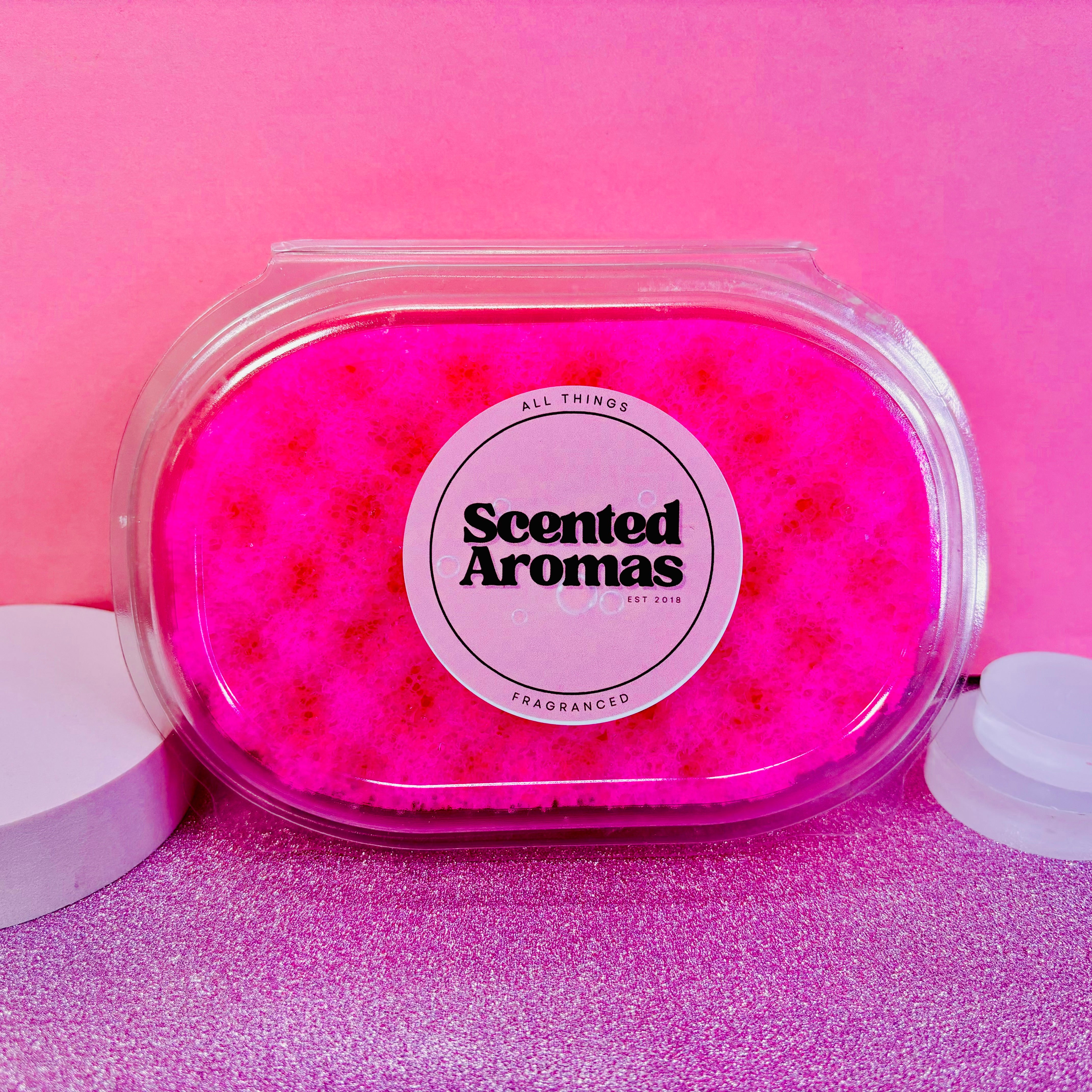 A clear plastic container holds the Pink Grapefruit Exfoliating Soap Sponge by The Soap Gal x against a pink background, evoking the refreshing scent of bright pink grapefruit, perfect for enhancing your skincare routine.