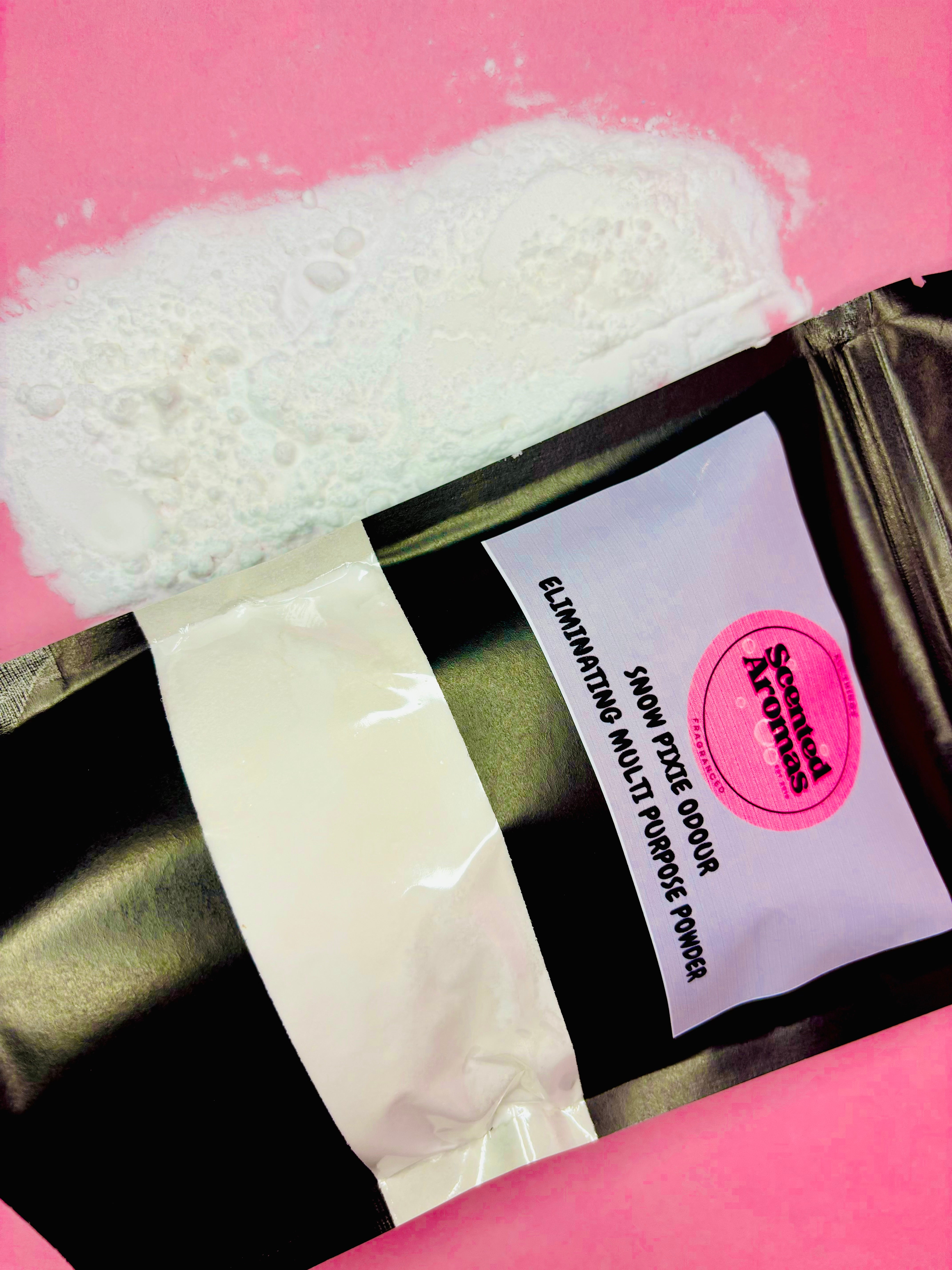 An open black package labeled "Snow Pixie Odour Eliminating Multi Purpose Powder 500g" from The Soap Gal x displays a spill of Snow Pixie scented white powder on a pink surface.