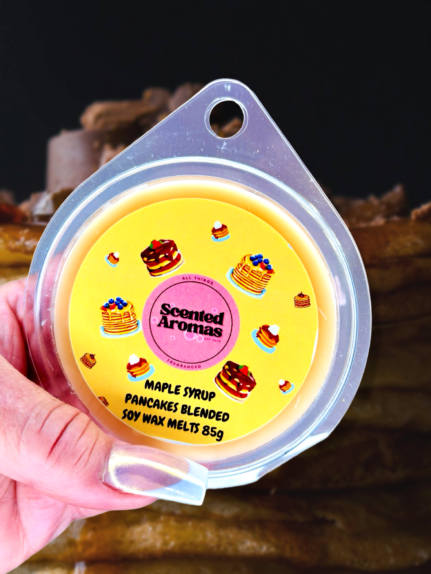 Close-up of a hand holding a container of The Soap Gal x's Maple Syrup Pancakes Wax Melts 85g, adorned with pancake illustrations on the lid. Enjoy the distinctive aroma of Maple Syrup Pancakes.