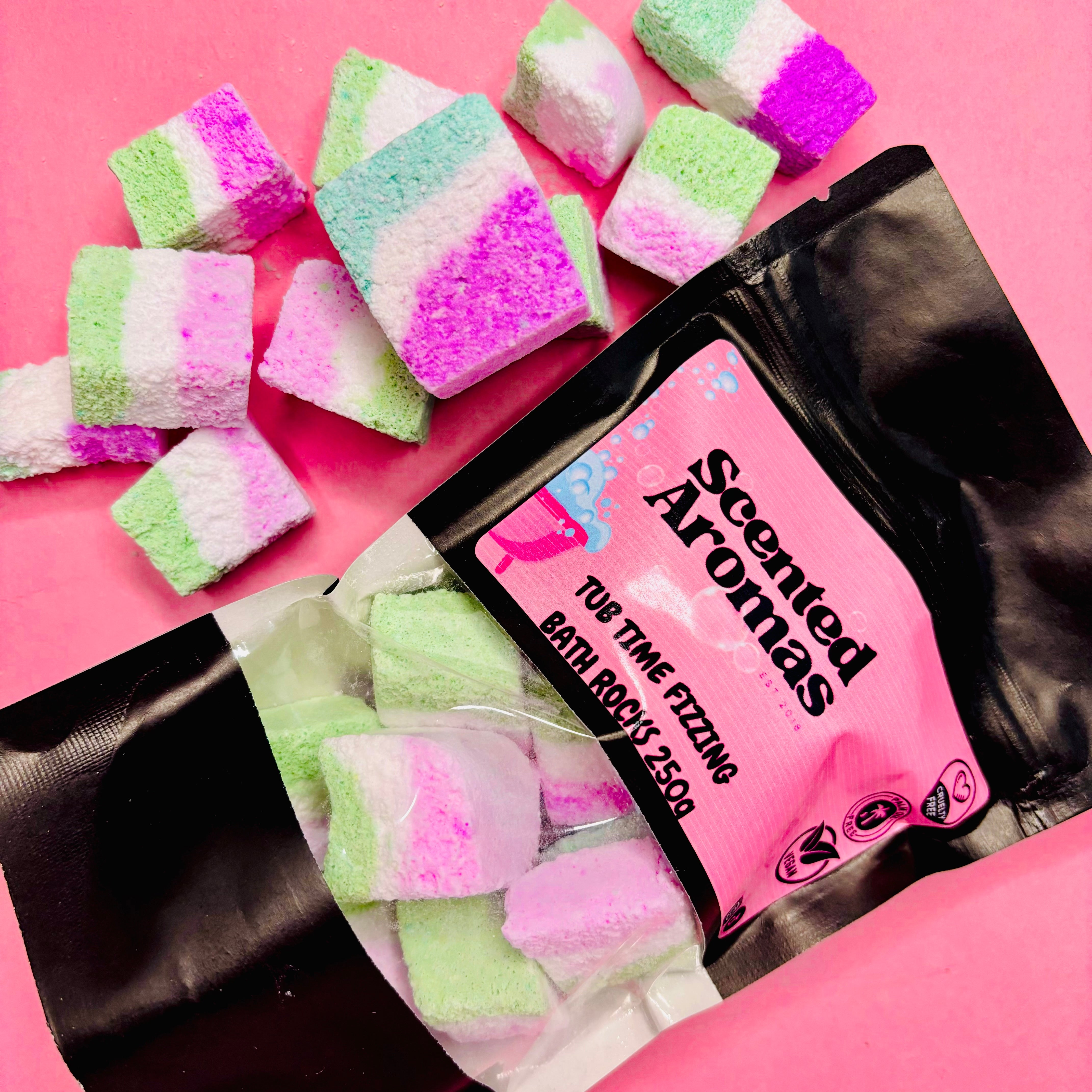 An open black pouch displays an array of colorful cube-shaped bath bomb rocks on a pink surface. The label reads "The Soap Gal x, Workin' 9-5 Relaxing Stress Reliever Bath Bomb Rocks," ideal for unwinding with scented bath products.