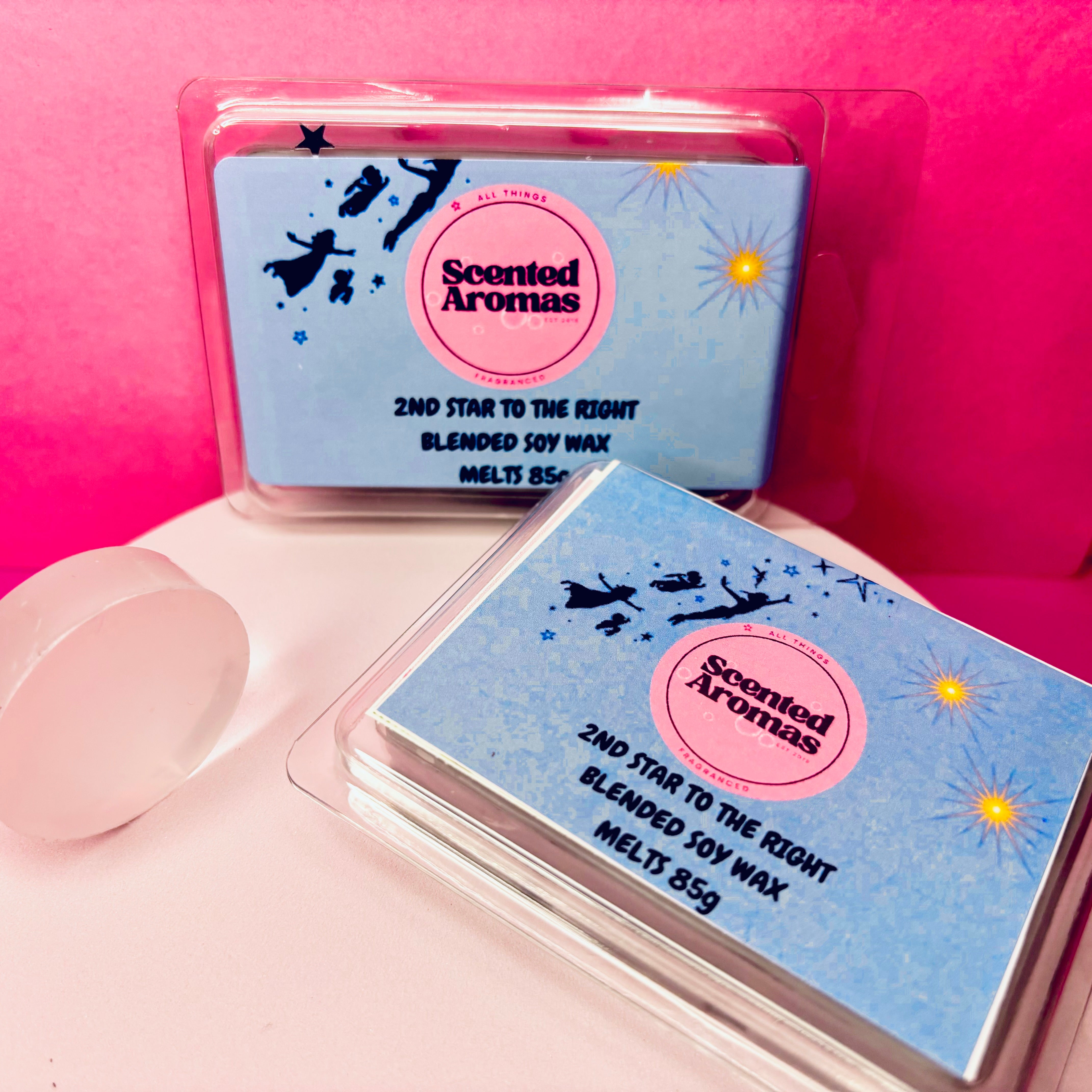 Two packs of "The Second Star to the Right" 85g soy wax melts from The Soap Gal x offer a magical fragrance experience with long-lasting aroma, presented against a pink backdrop.