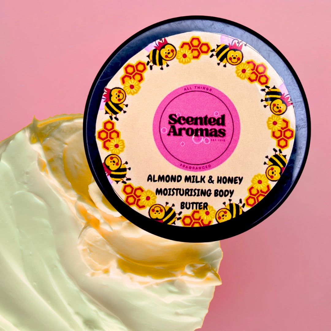 A 100ml container of Scented Aromas Almond Milk and Honey Body Moisturising Butter, cruelty-free, is on a pink background with a cream swirl underneath.