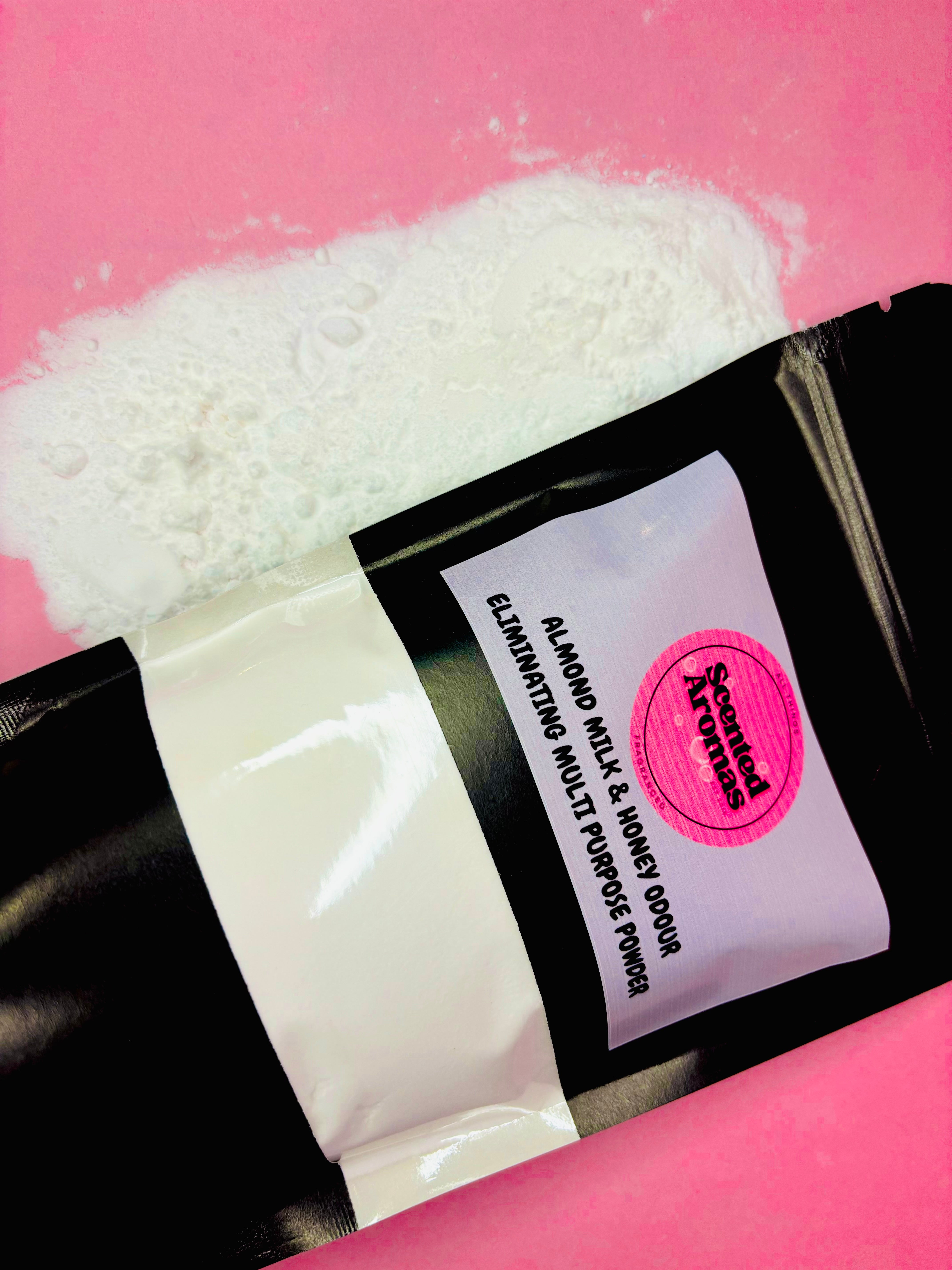 A pouch of The Soap Gal x Almond Milk and Honey Multi Purpose Freshener 500g is spilling on a pink surface, releasing a soothing aroma that fills the air with its gentle home scent.