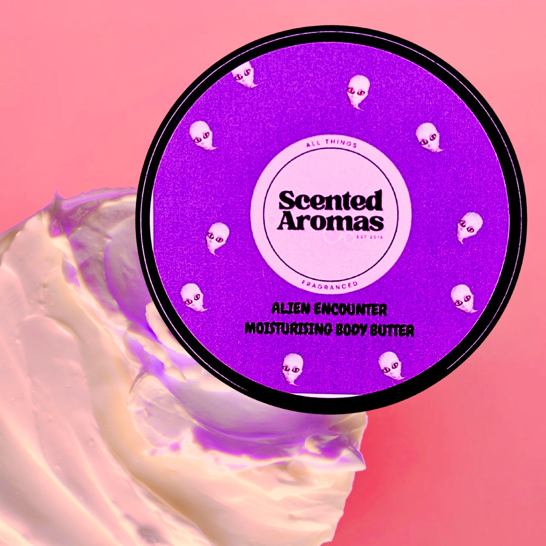 A 100ml "Alien Encounter Body Moisturising Butter" from Scented Aromas rests on a pink background beside a cream smear, delivering soothing skin nourishment and lasting fragrance.