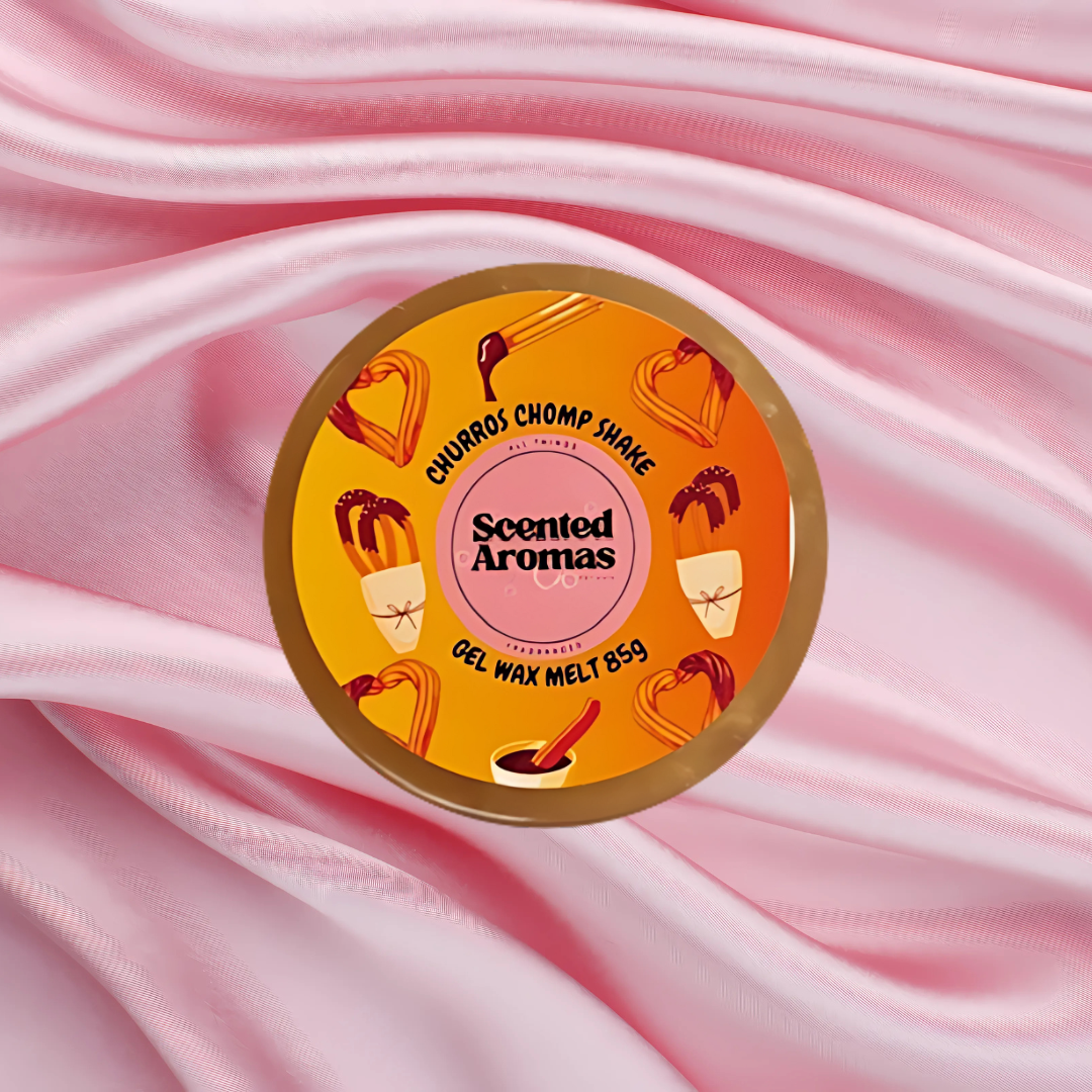 A circular container of Fresh Churros Magical Gel Wax Melts 85g by The Soap Gal x, adorned with an orange label showcasing ice cream illustrations, rests on pink satin fabric. Indulge in the opulence of enduring home fragrances with our luxurious gel wax melts.