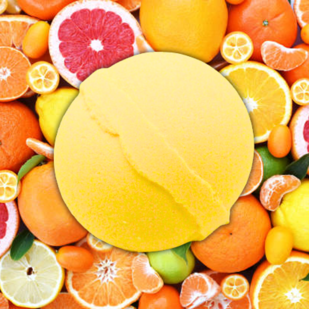 A collection of assorted citrus fruits in the background with a large, yellow, circular Citrus Crush Jumbo Bath Bomb from The Soap Gal x in the center.