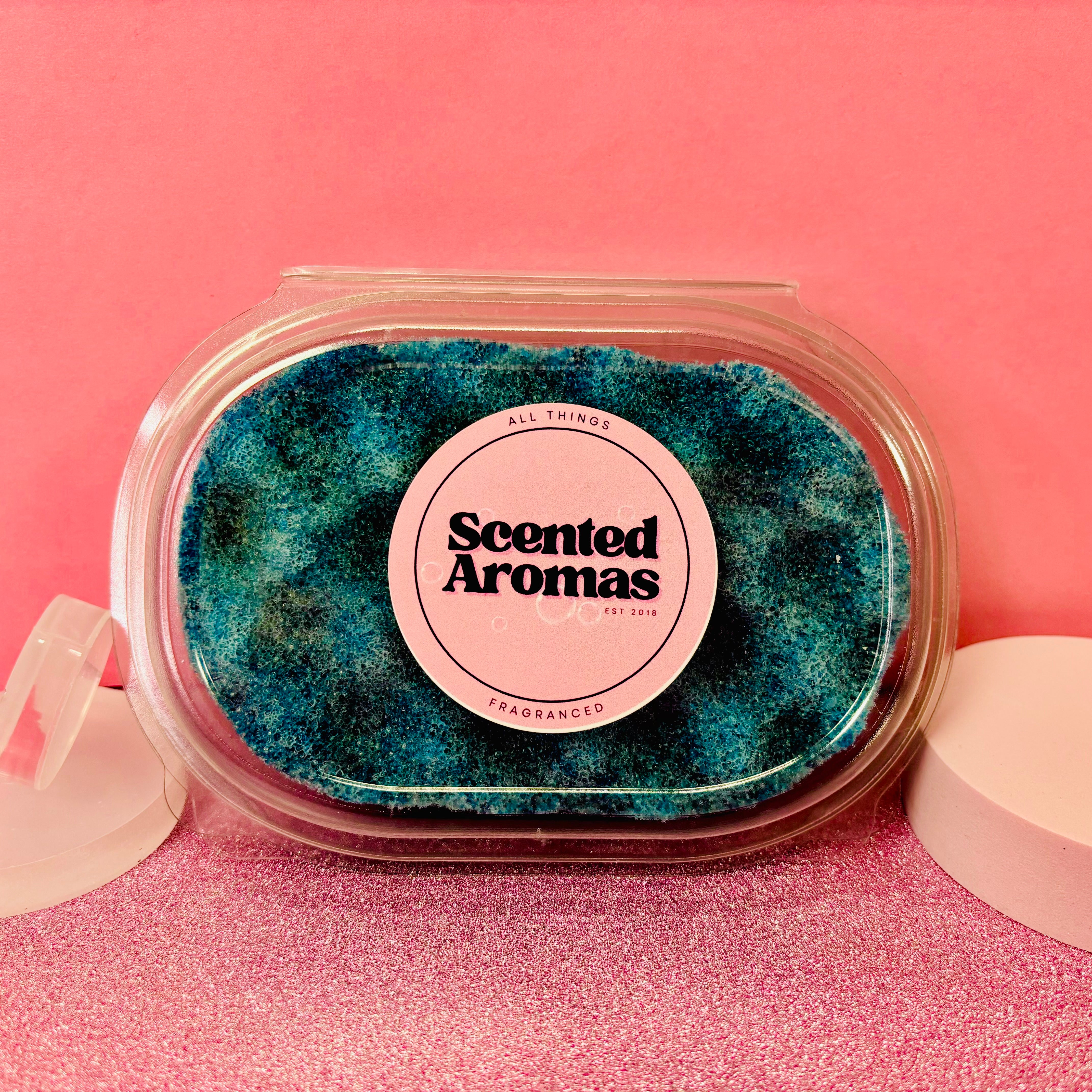 An Olympia Exfoliating Soap Sponge by The Soap Gal x, designed to invigorate any skincare routine with a refreshing touch, is showcased against a pink background.