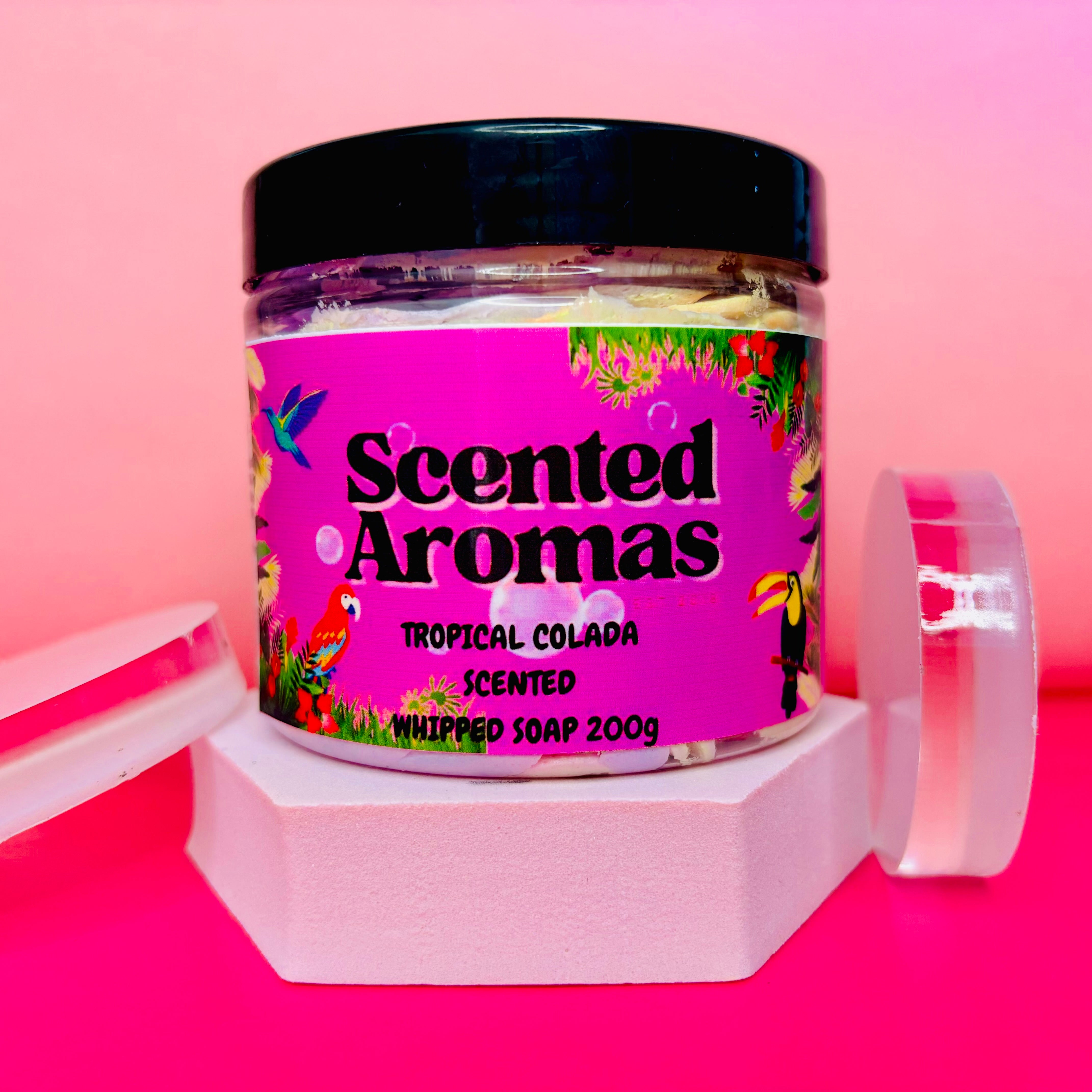 A jar of The Soap Gal x Unicorn Fluff Whipped Soap Shave Butter, weighing 200g and exuding a delightful tropical colada scent, stands out against a pink background.