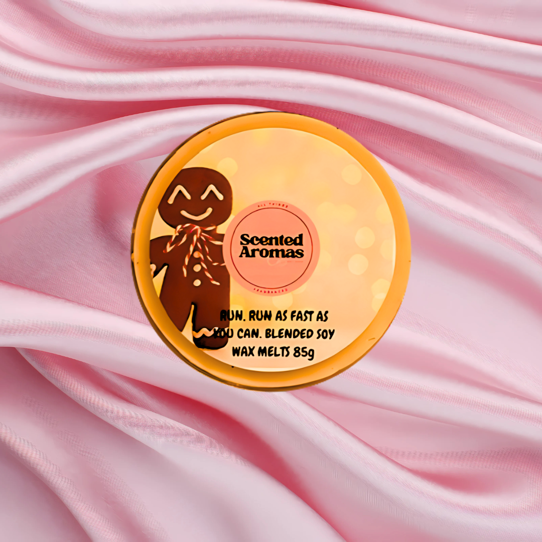 Round tin of The Soap Gal x "Run Run As Fast As You Can Gingerbread Wax Melts" crafted from a blended soy wax, set against a pink fabric background. Text reads: "Run, run as fast as you can. Blended soy wax melts 85g.