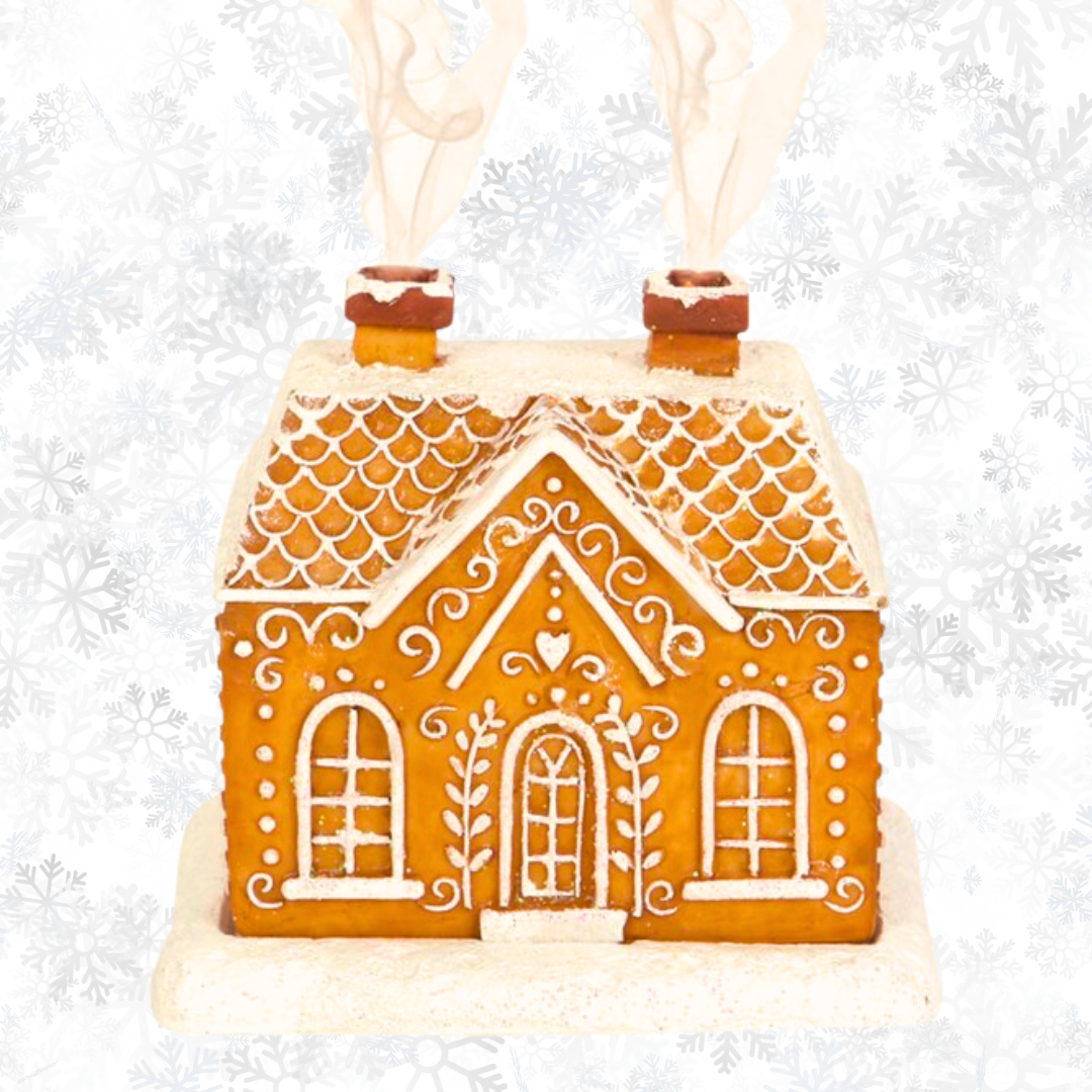 This charming Gingerbread House Incense Cone Burner by The Soap Gal x showcases intricate white icing details and two chimneys, complemented by a snowflake-patterned backdrop. An ideal addition for infusing any space with festive holiday decor.