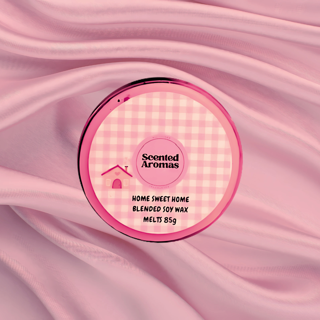 A round container of "Home Sweet Home Wax Melt | 85g" by The Soap Gal x, with a pink gingham pattern, rests on soft pink fabric. This charming soy wax melt infuses any space with a comforting home fragrance.