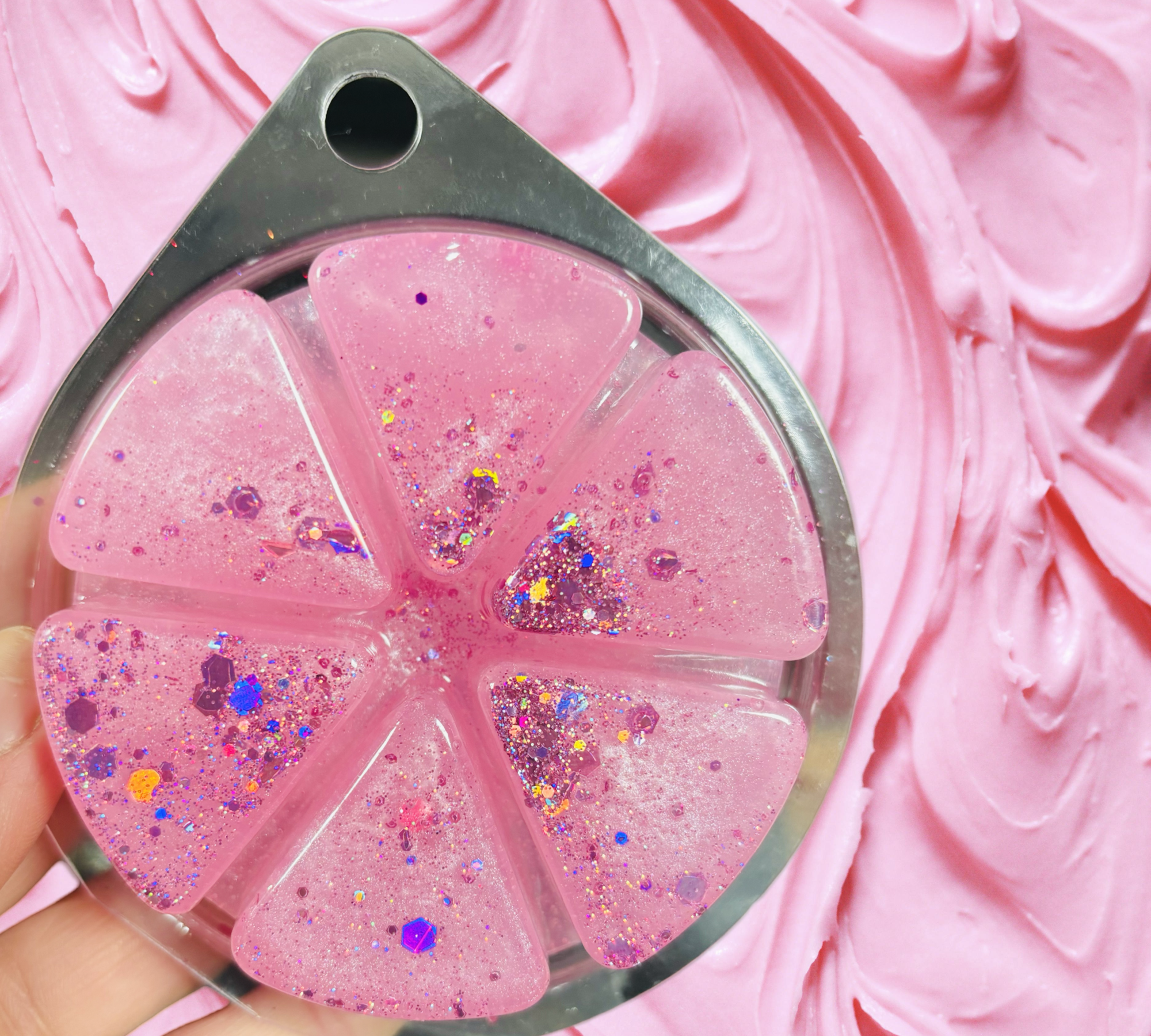 Pink, glittery wedges from the Scented Aromas Valentines Gift Set Bundle, reminiscent of a Birthday Cake scented bath bomb, are arranged in a circular silver mold against a textured pink background.