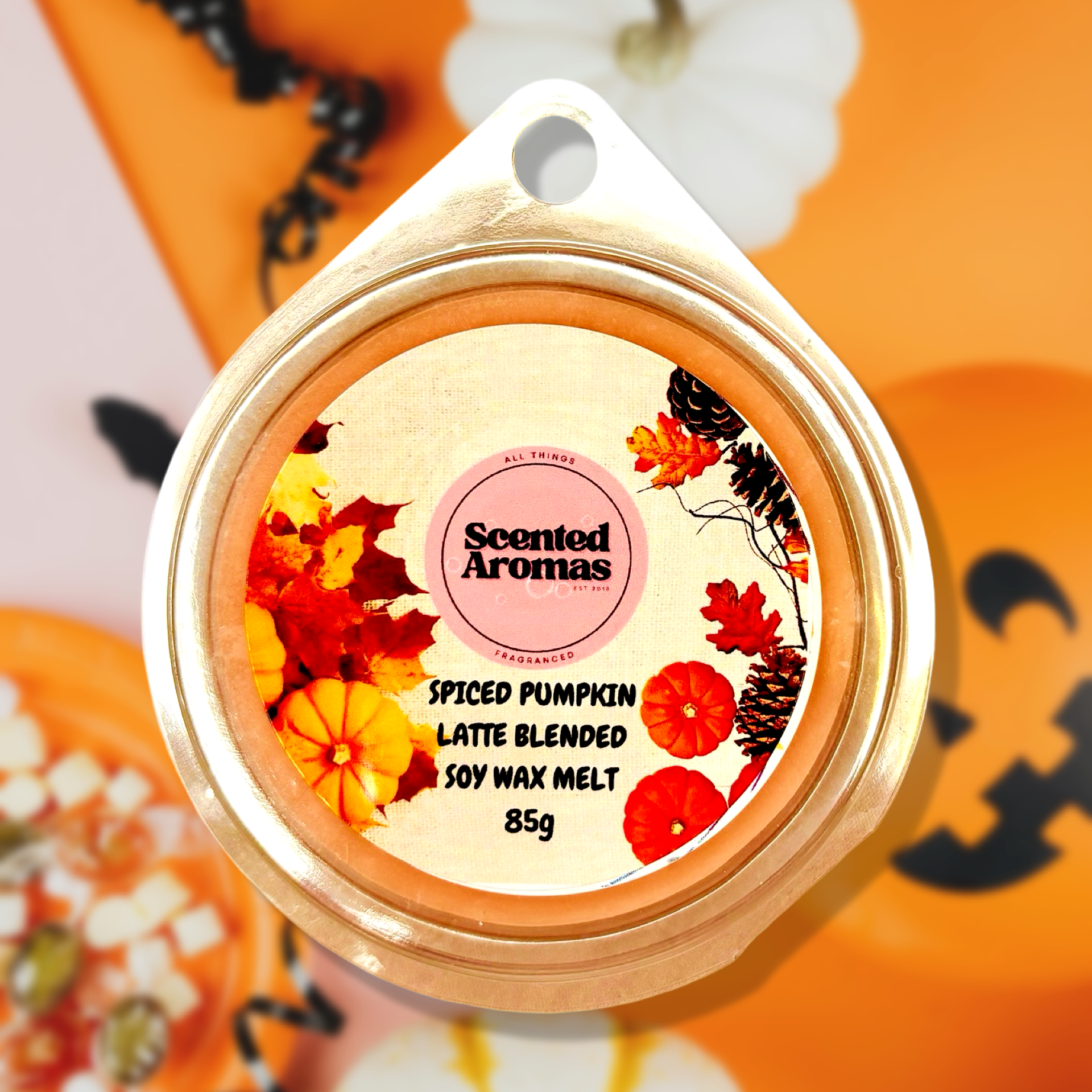 An 85g package of Pumpkin Spice and All Things Nice Wax Melts by The Soap Gal x is made from a smooth soy wax blend. This product features a festive autumn leaf design and offers a long-lasting fragrance. In the background are vibrant orange and white pumpkins, along with a cheerful jack-o'-lantern face.