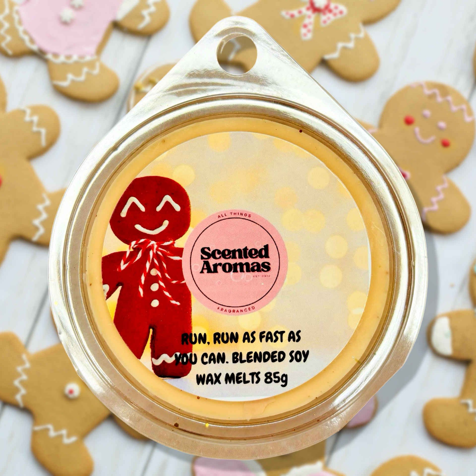 A round container of The Soap Gal x's "Run Run As Fast As You Can" gingerbread wax melts, crafted from a soy wax blend and featuring a charming gingerbread man design. In the background, gingerbread cookies add a festive touch to this aromatic delight.