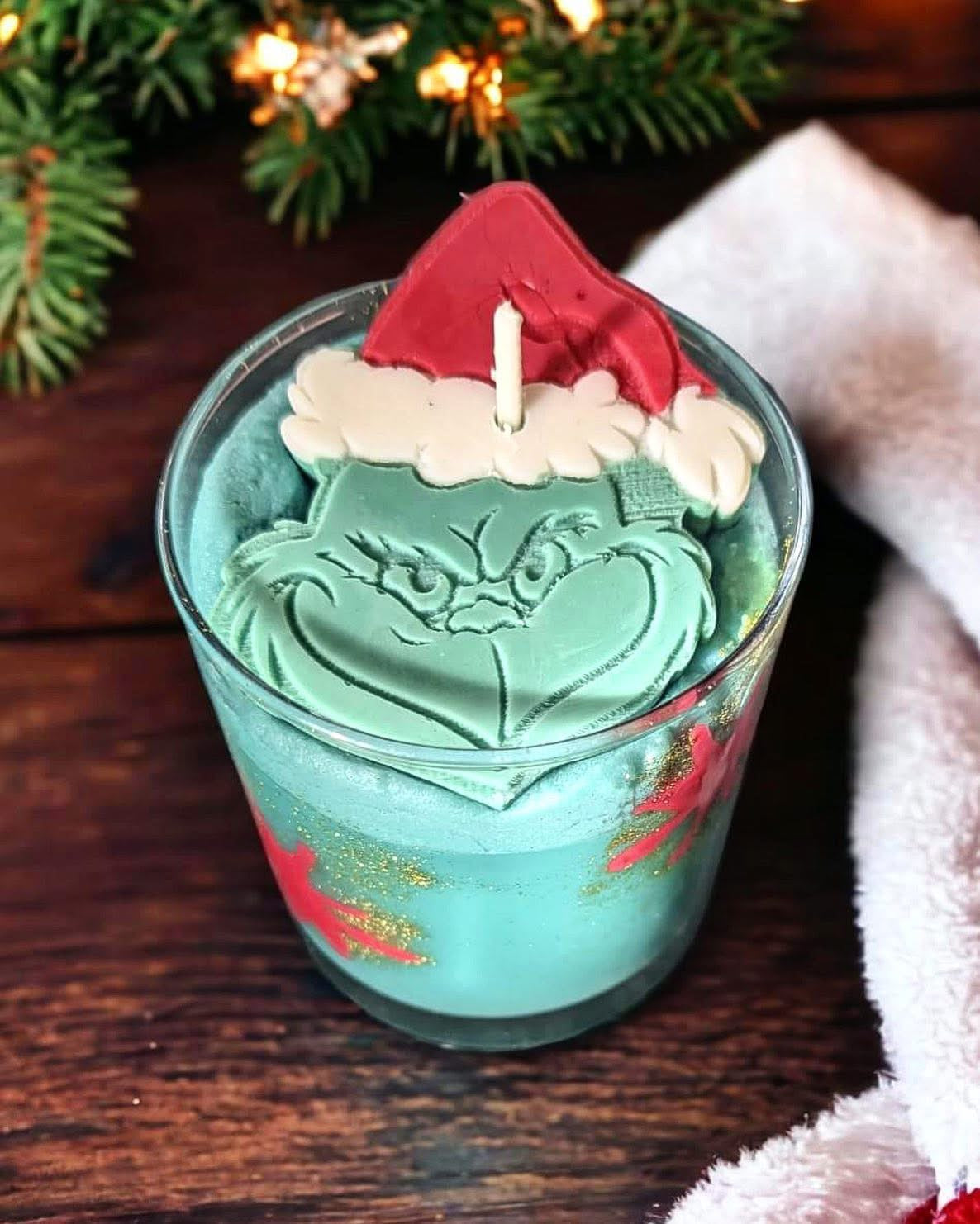 Introducing The Grinch Candle by Scented Aromas, our limited edition festive candle featuring a wax figure with a green hue and Santa hat, inspired by the beloved cartoon character. This unique candle is housed in a winter-themed glass holder, emitting a long-lasting fragrance that keeps your home cozy and cheerful all season long.