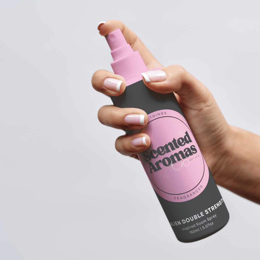 A hand holds a spray bottle with a pink label of "Baby Powder Room Spray 150ml" by The Soap Gal x, angled slightly upward, perfect for eliminating odors with its gentle Baby Powder fragrance.