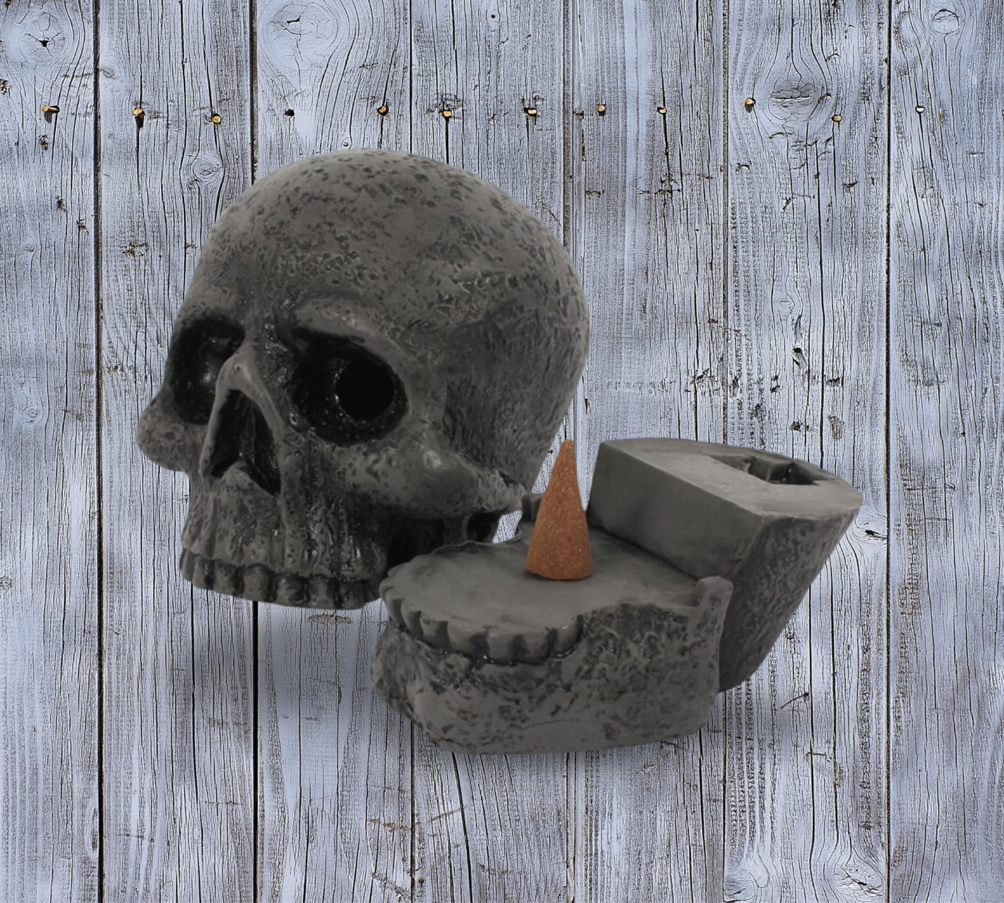 A Skull Incense Cone Burner by The Soap Gal x, featuring a removable lid and stone finish, presents a single cone incense emitting a soothing aroma against a rustic wooden backdrop.