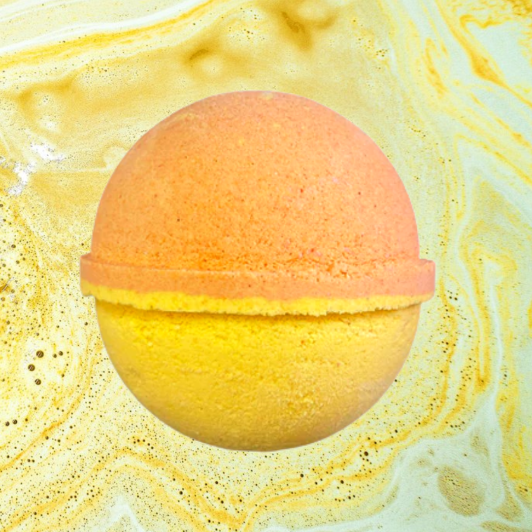 A round, half-orange and half-yellow Men's Creed Aventus Bath Bomb by The Soap Gals rests against a swirling, marbled yellow and brown background.