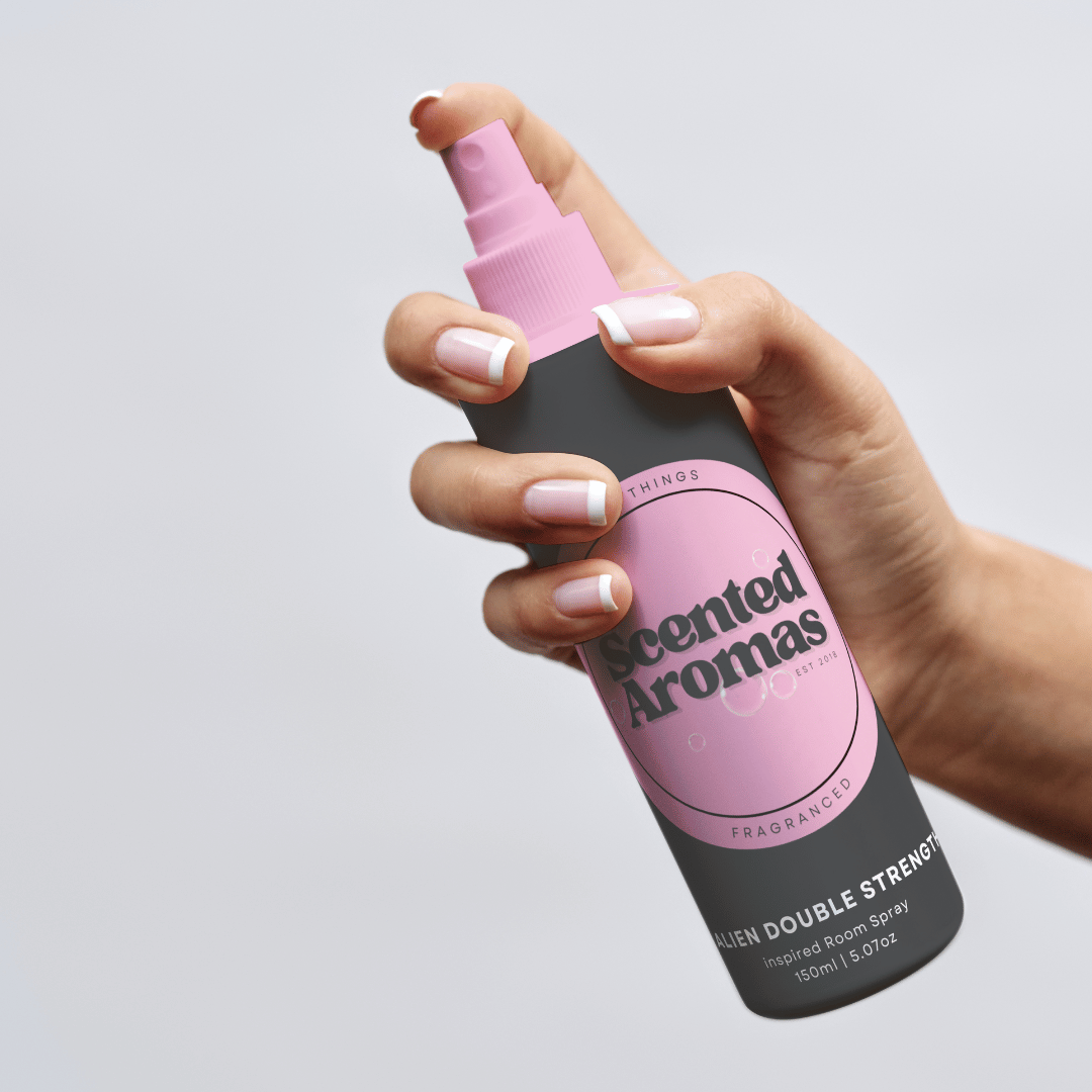 A hand with French manicured nails holds a black and pink bottle labeled "Scented Aromas," ideal for releasing a refreshing citrus scent or serving as an insect repellent, ingeniously doubling as Citronella Room Spray 150ml.