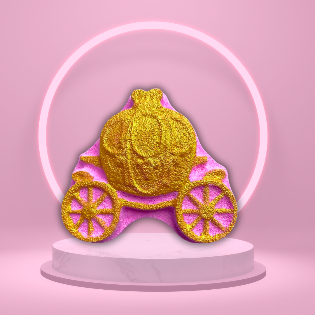 A golden Fairy Tale Carriage Bath Bomb by The Soap Gal x is displayed on a pedestal with a pink circular light in the background, exuding a whimsical charm reminiscent of a luxurious spa experience.