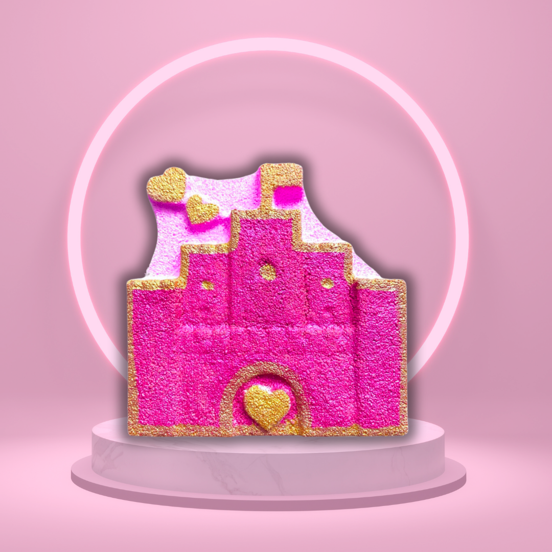 A pink and gold sandcastle, reminiscent of The Soap Gal x Castle of Dreams Bath Bomb from the magical collection, sits on a white circular pedestal against a pink background with a pink halo light.