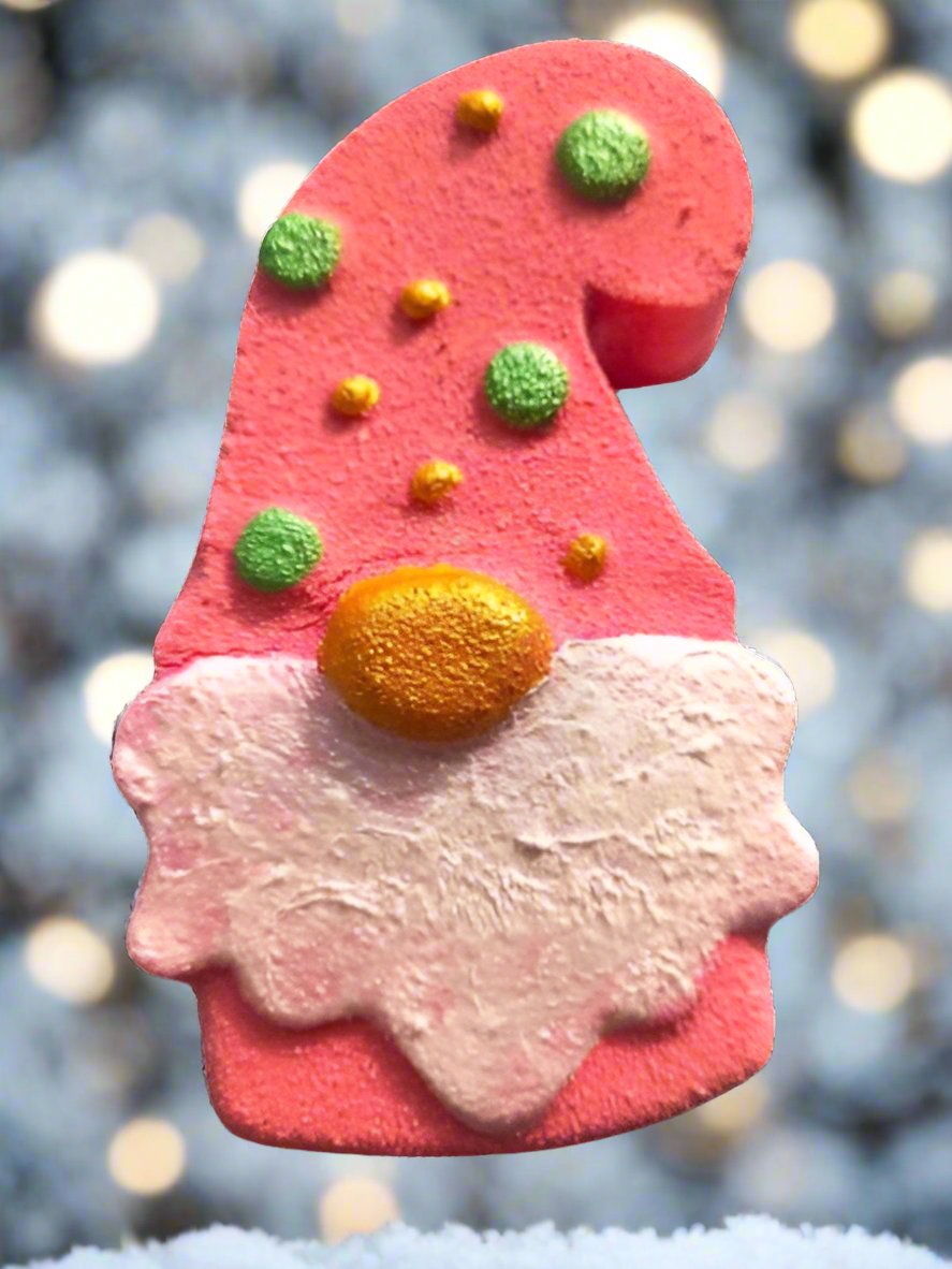 A whimsical, handmade pink Santa hat-shaped cookie, adorned with green and yellow decorations and a white icing pattern, sits against a blurred, snowy background. This delightful treat feels as special as A Christmas Gonk Bath Bomb from Scented Aromas.