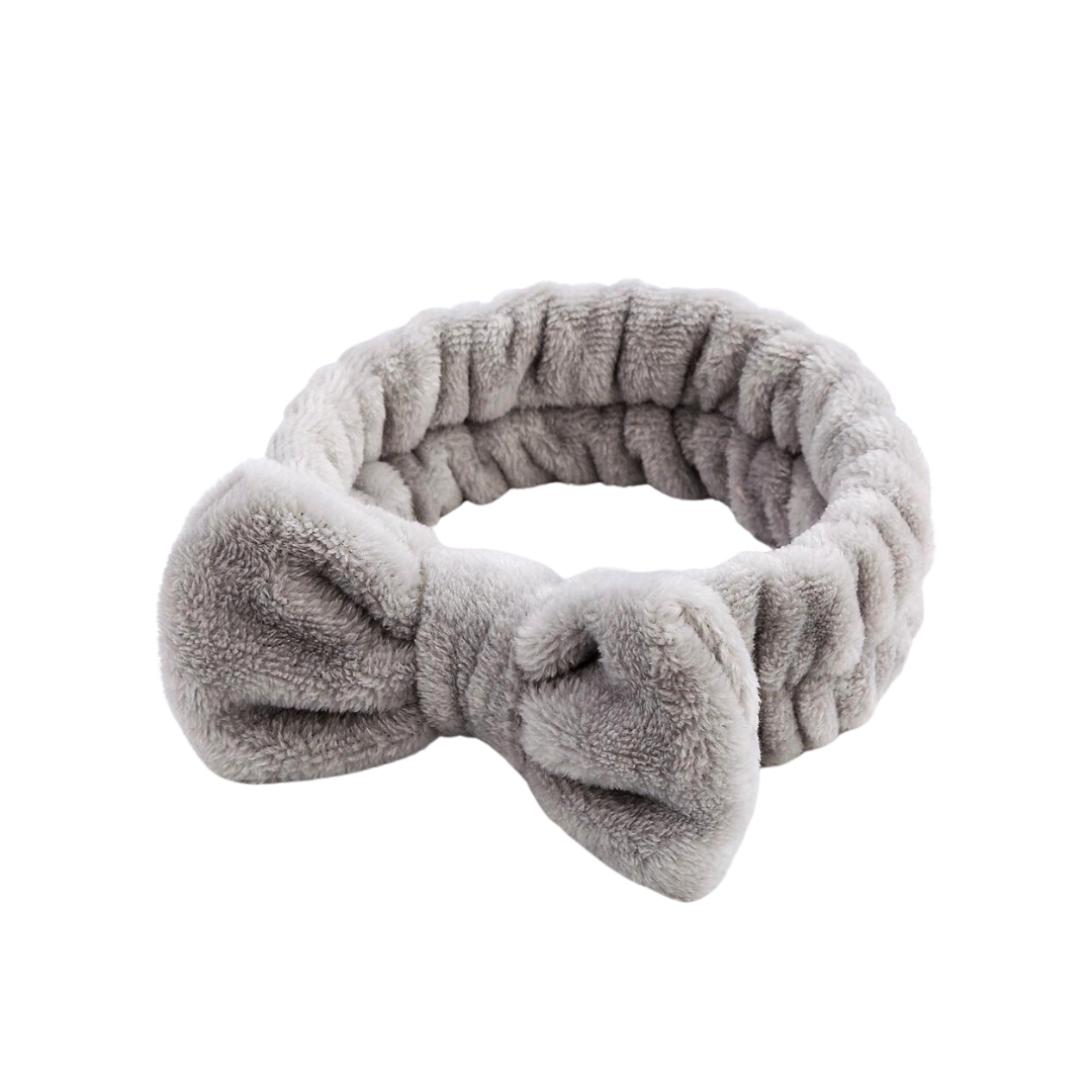 The Grey Fluffy Bow Headband by The Soap Gal x, made from elastic material, is an ideal addition to your skincare routine. This soft, plush gray headband showcases a delightful bow design on a white background.