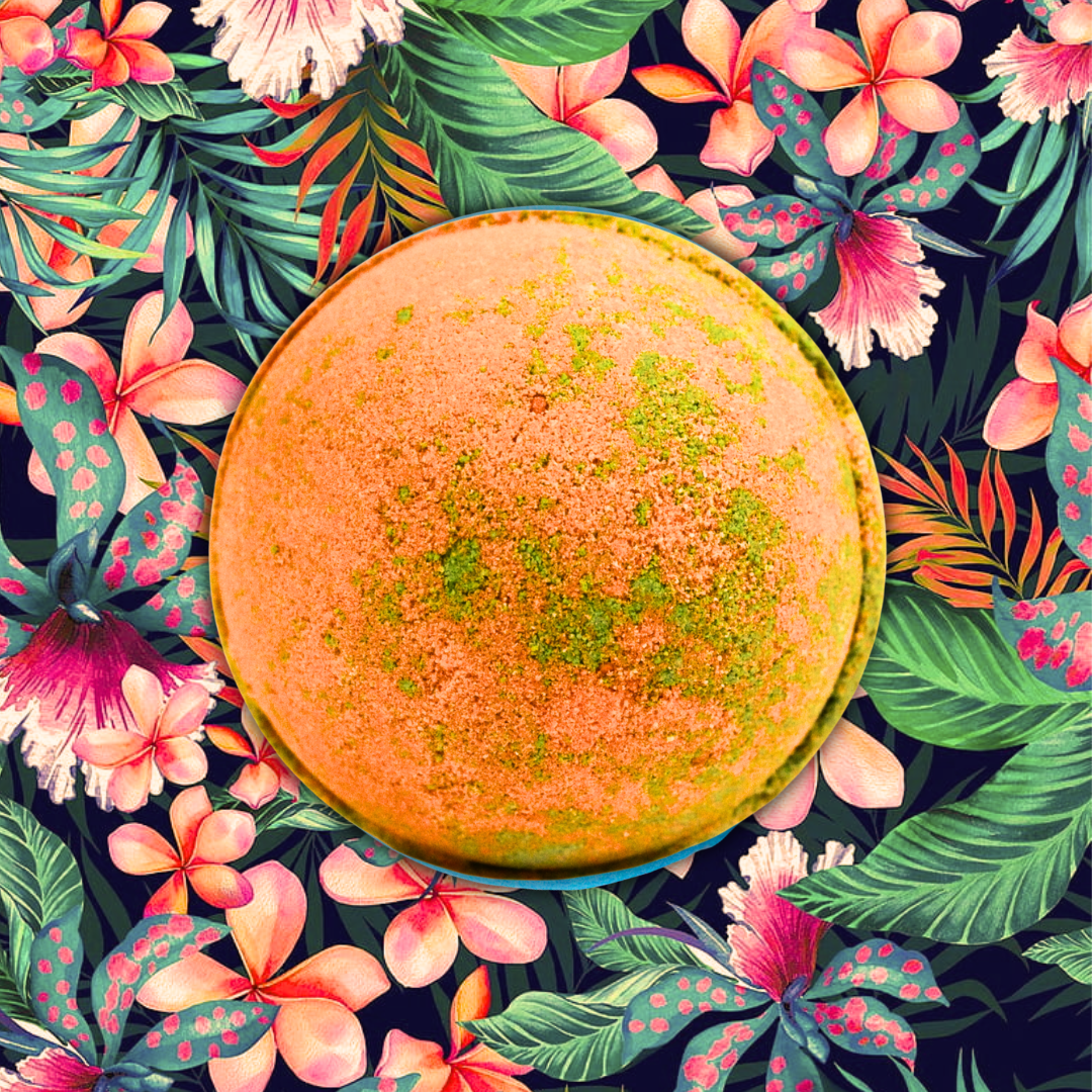 A vibrant, round Hawaiian Mango Jumbo Bath Bomb with an orange and green mottled surface is centered against a colorful, floral background with various flowers and tropical leaves, evoking the ultimate getaway experience in a tropical paradise.