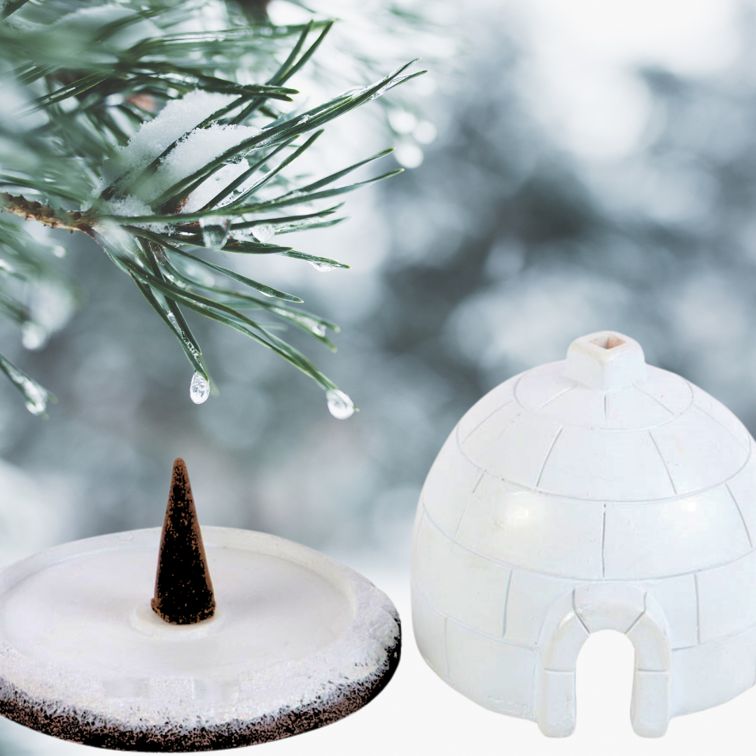 A close-up of a snow-covered pine branch with dripping water creates a serene, holistic atmosphere next to The Soap Gal x Igloo Incense Burner and a snow-laden traffic cone, enhancing the scene with distinctive winter decor.